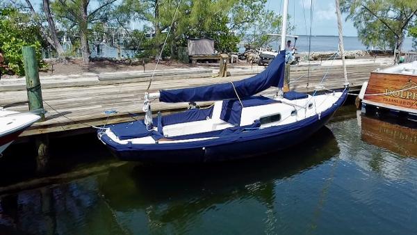 Vintage 1968 Sailboat 24 docked by a wooden pier, surrounded by trees and calm water.