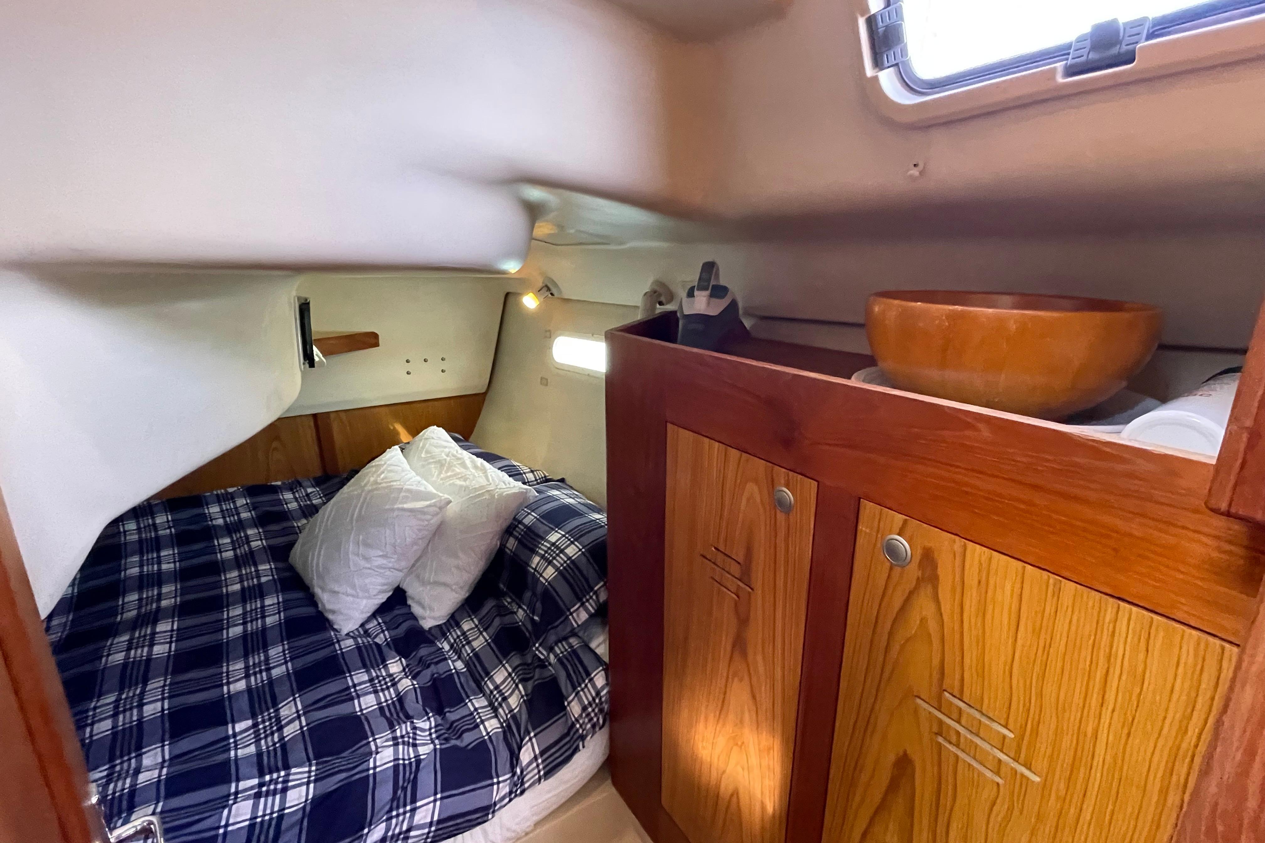 Cozy cabin interior of 2000 Hunter 340 sailboat with plaid bedding and wooden cabinetry.