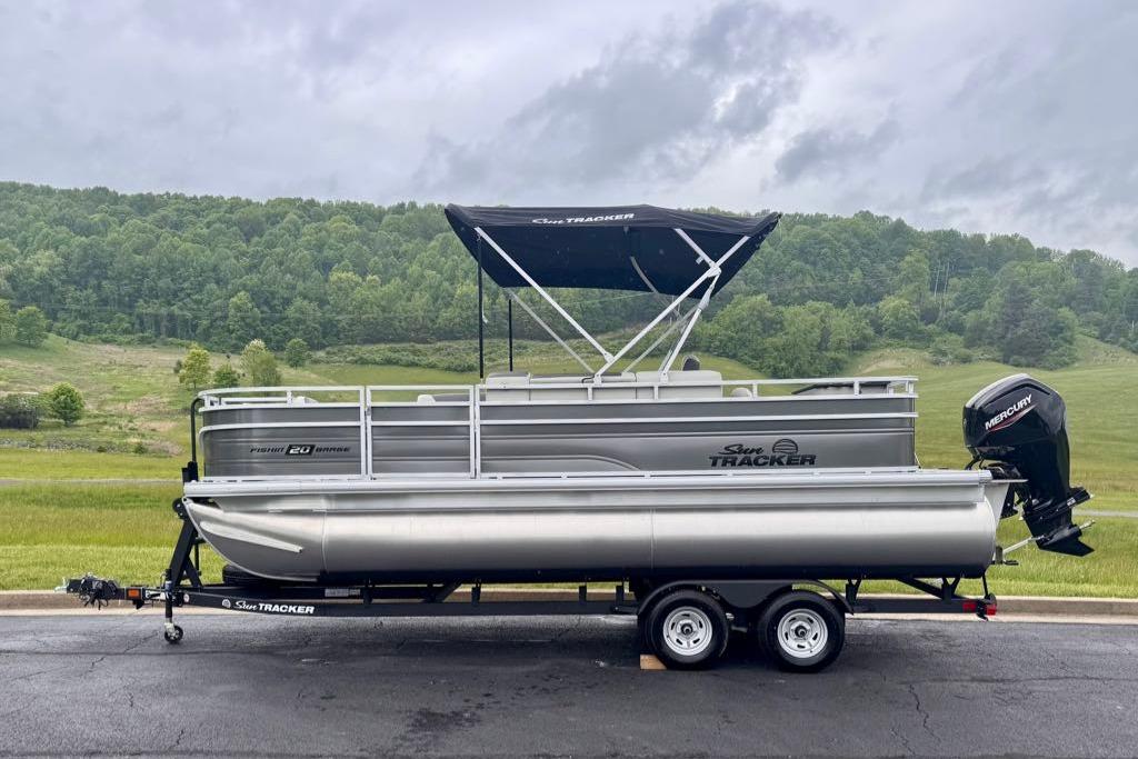 2026 Sun Tracker Fishin' Barge 20 DLX pontoon boat on trailer, scenic background.