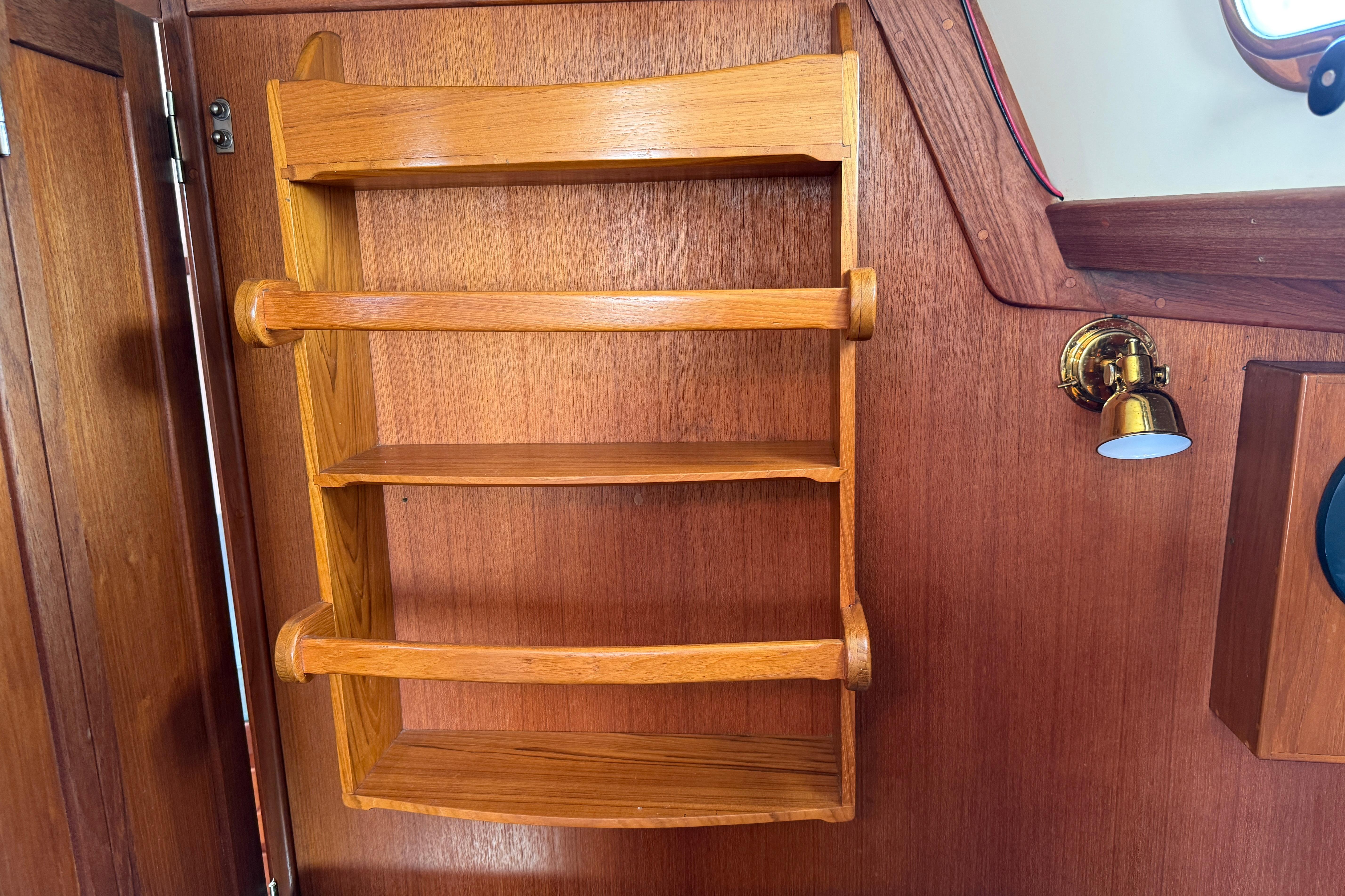 Wooden shelves inside a 1997 Tartan 3800 boat, featuring a brass wall light.
