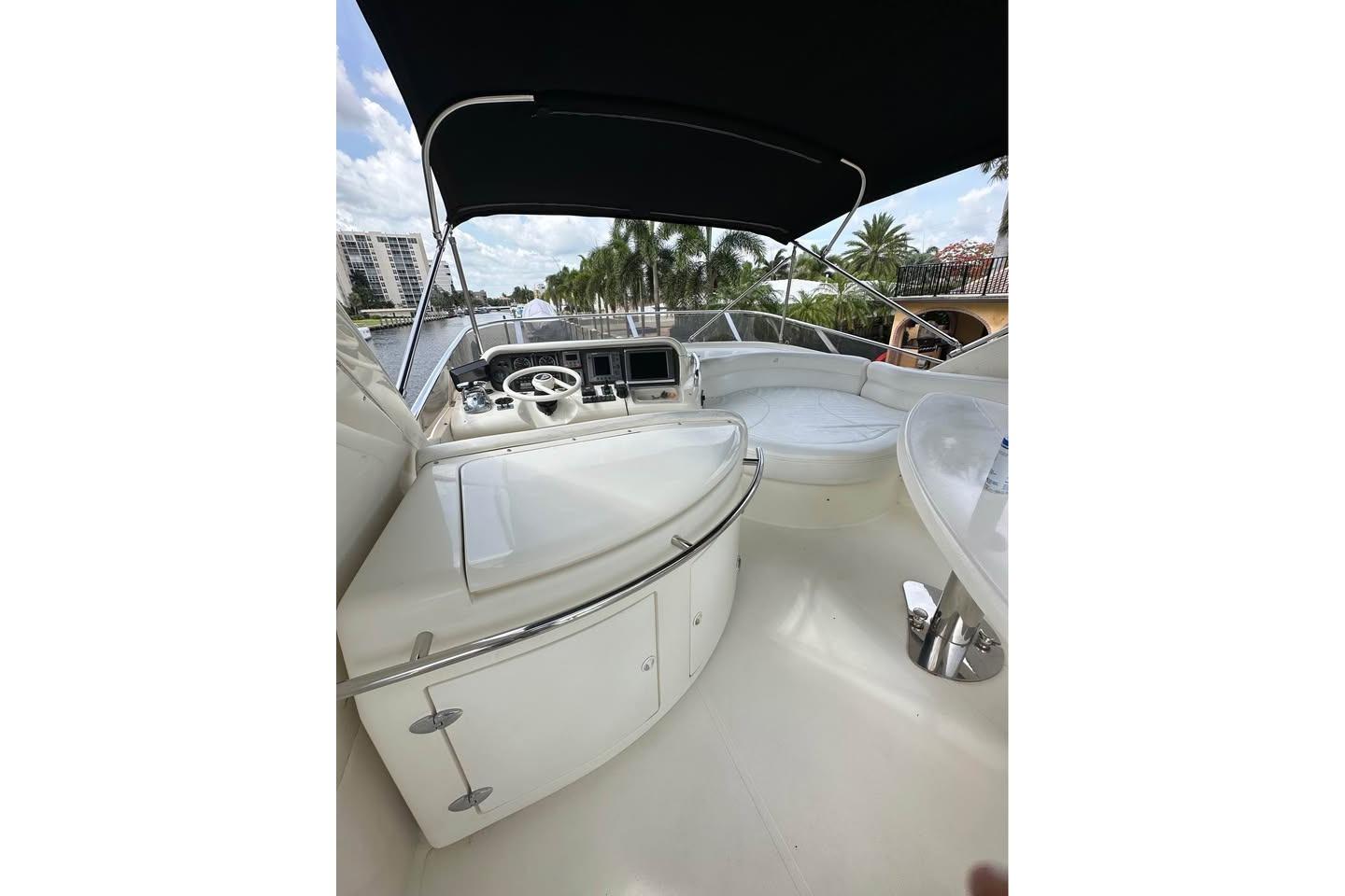 2004 Azimut 55E yacht cockpit with steering wheel, seating, and canopy, docked by palm trees.