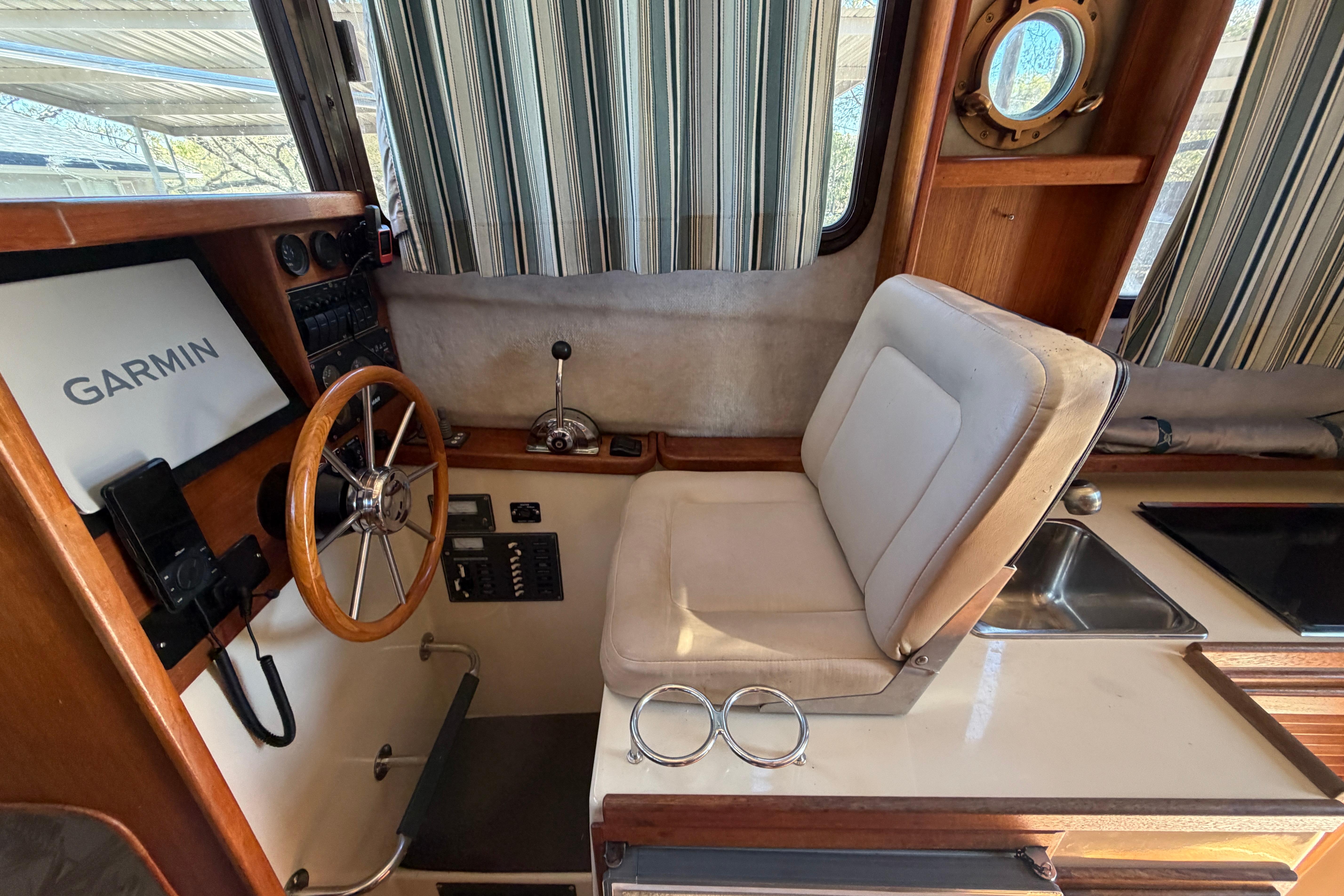 2008 Ranger Tugs R-25 helm with Garmin navigation, wooden steering wheel, and striped curtains.