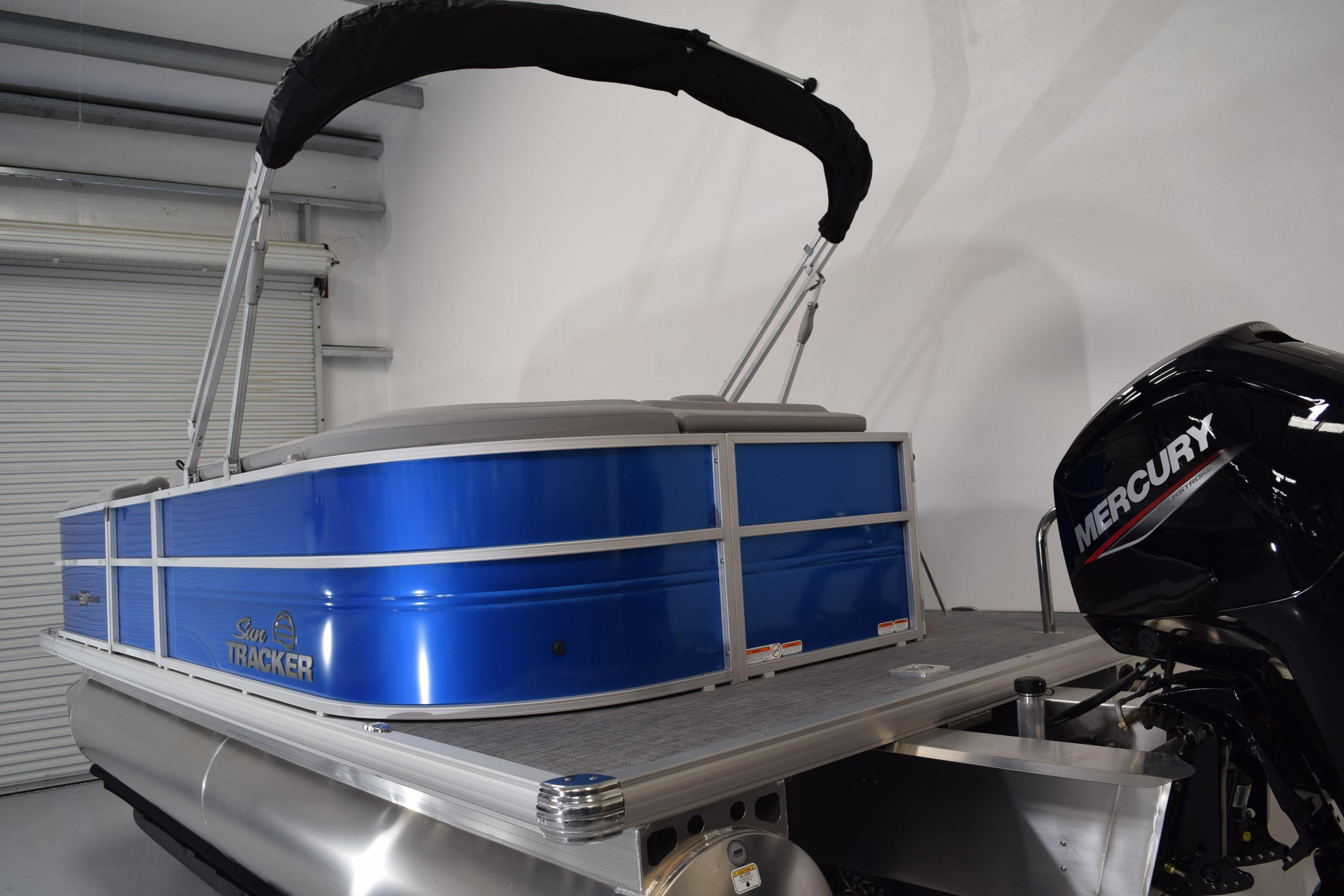 2026 Sun Tracker Party Barge 20 DLX pontoon boat with Mercury engine in a garage.