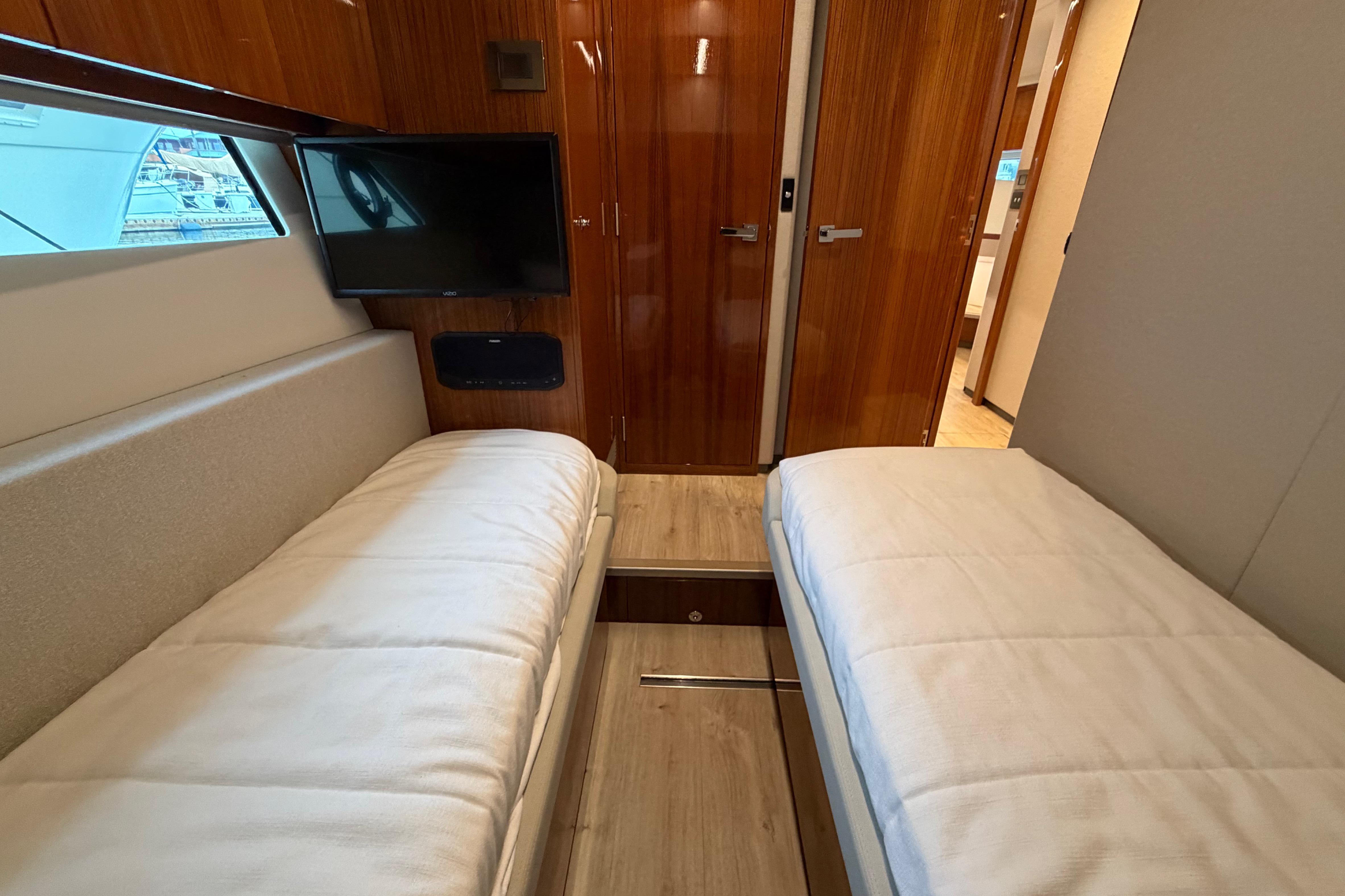 Interior of 2023 Riviera 645 SUV yacht with twin beds and a wall-mounted TV.