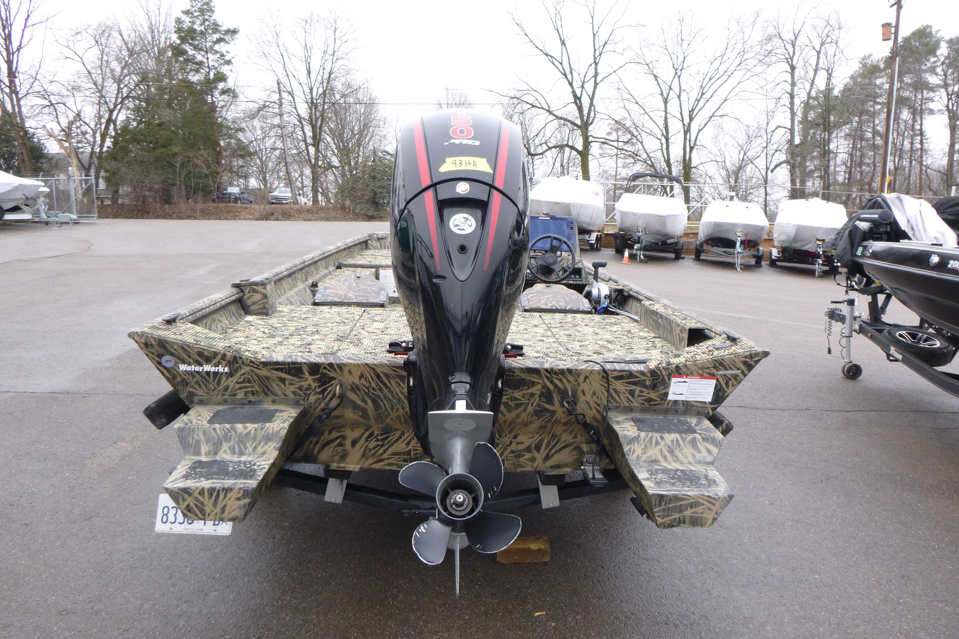 2024 Lowe Roughneck 2070 boat with camouflage design and outboard motor in a parking lot.