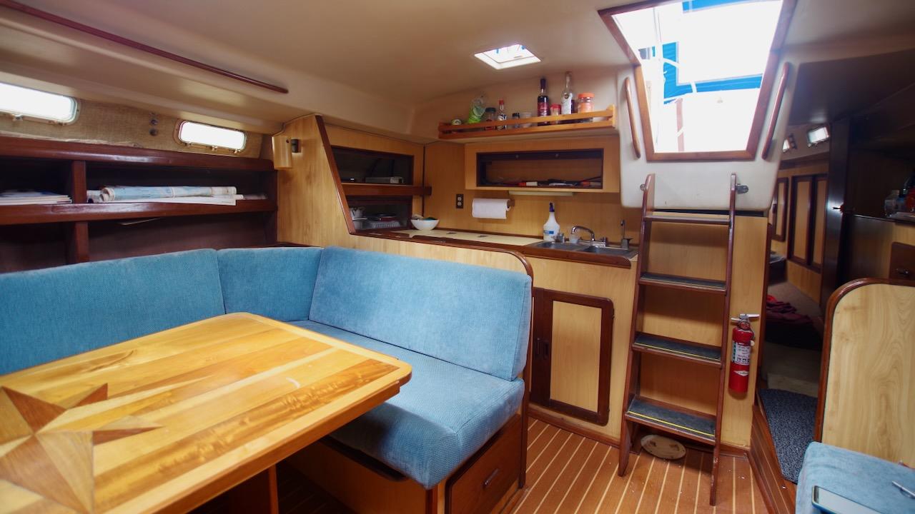 1981 Morgan Out Island 41 yacht interior with blue seating, wooden table, and compact kitchen.