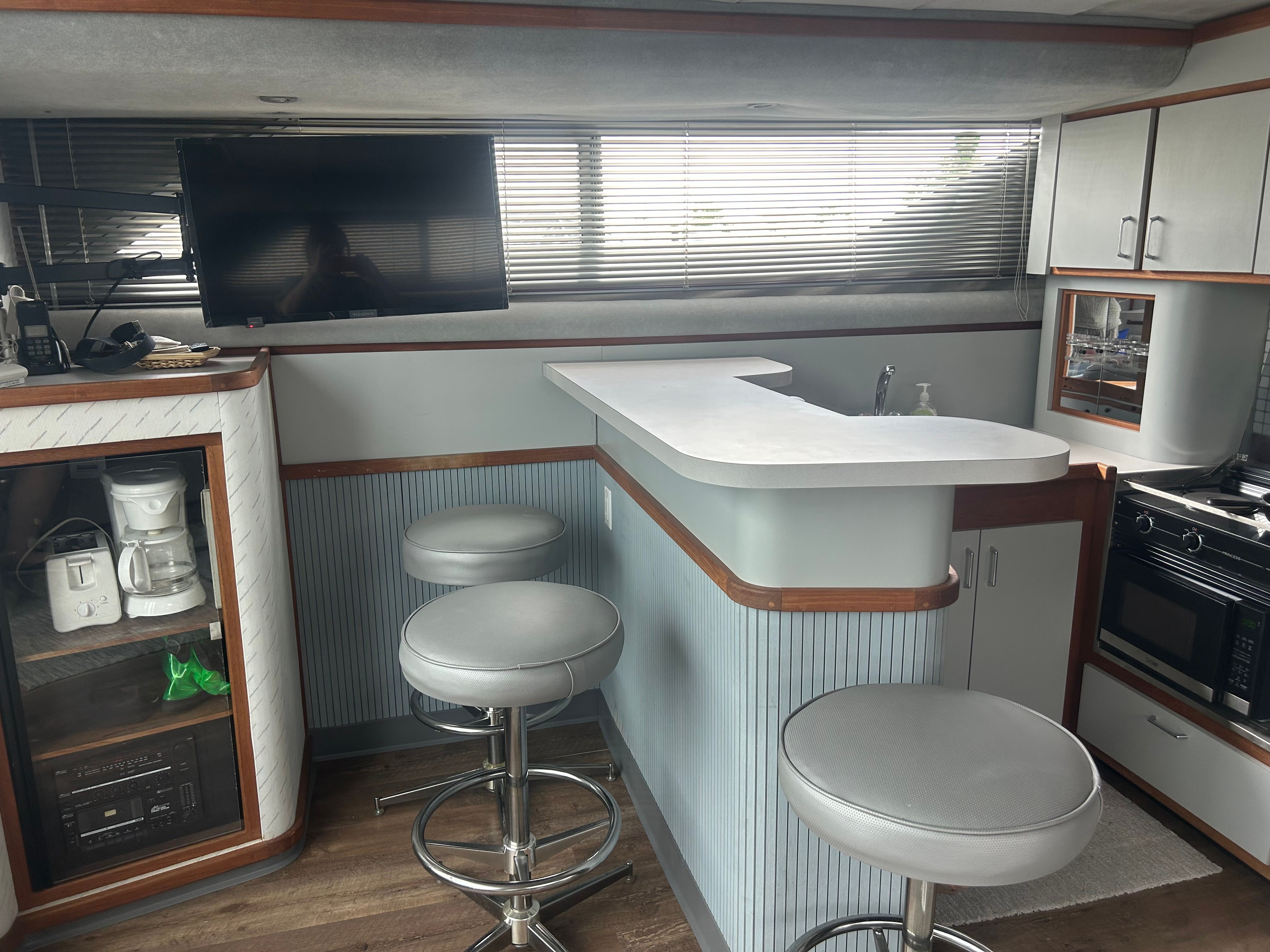 Interior of a yacht with a bar, stools, TV, and kitchen area.