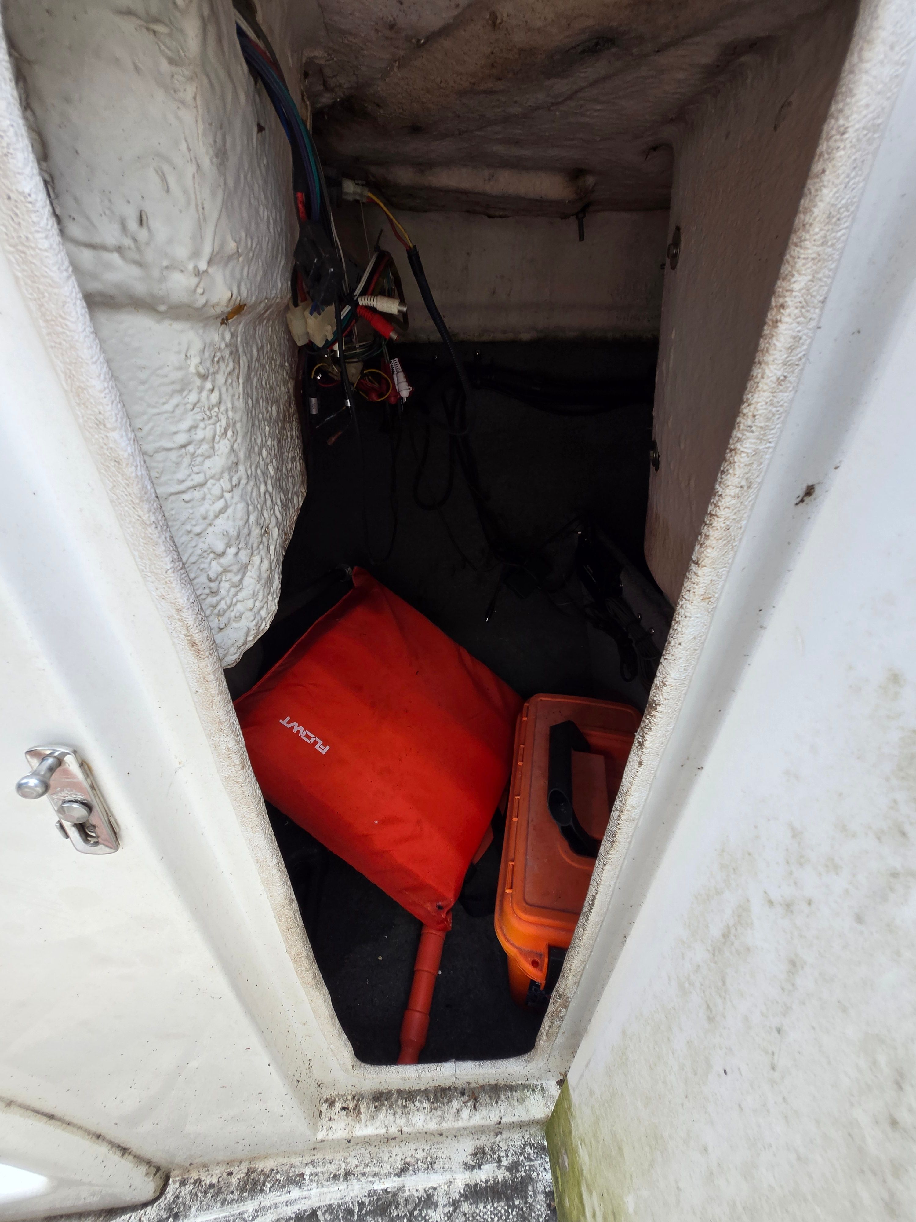 A storage compartment inside a boat with an orange container and wires.