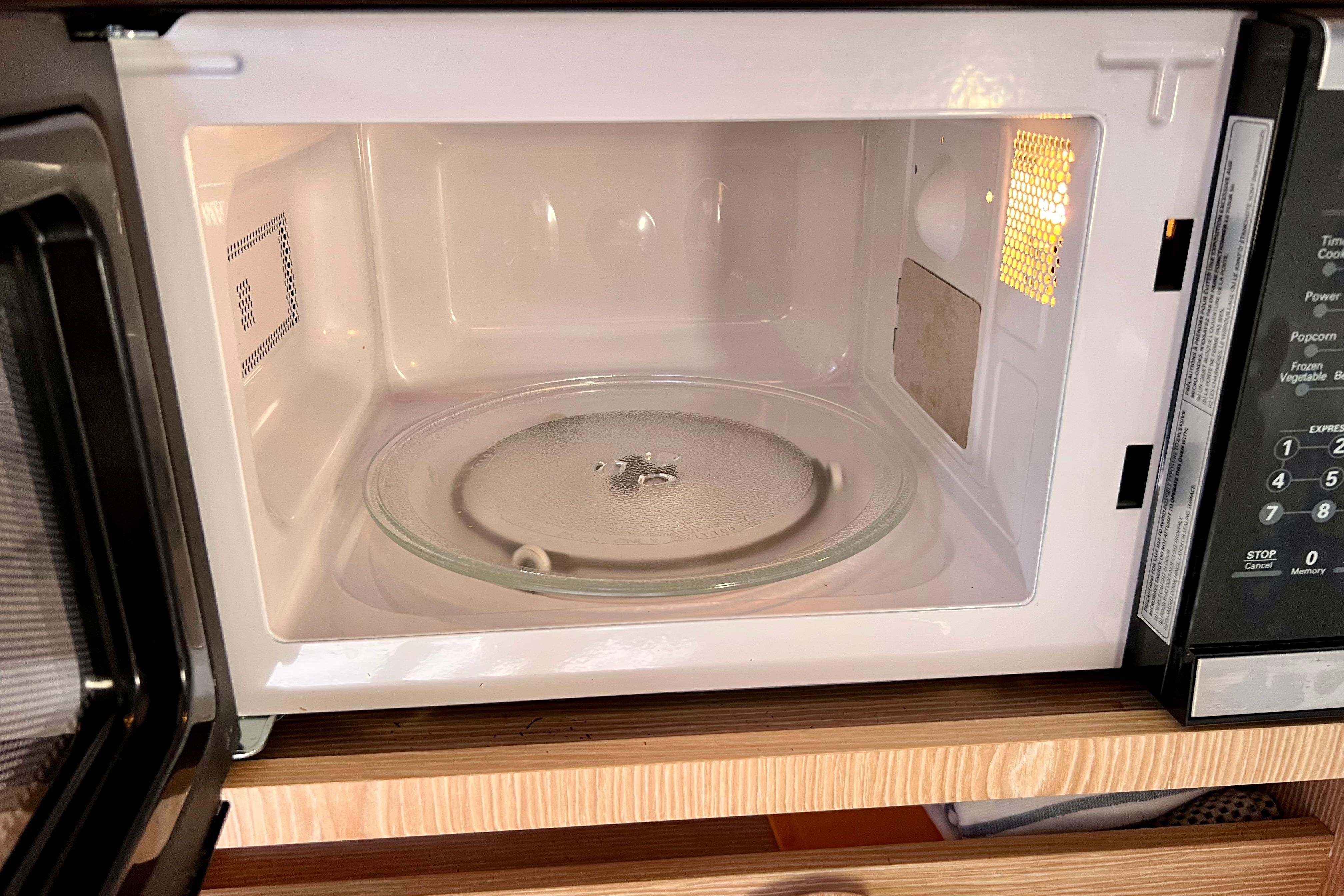 Open microwave oven with glass turntable on wooden shelf.