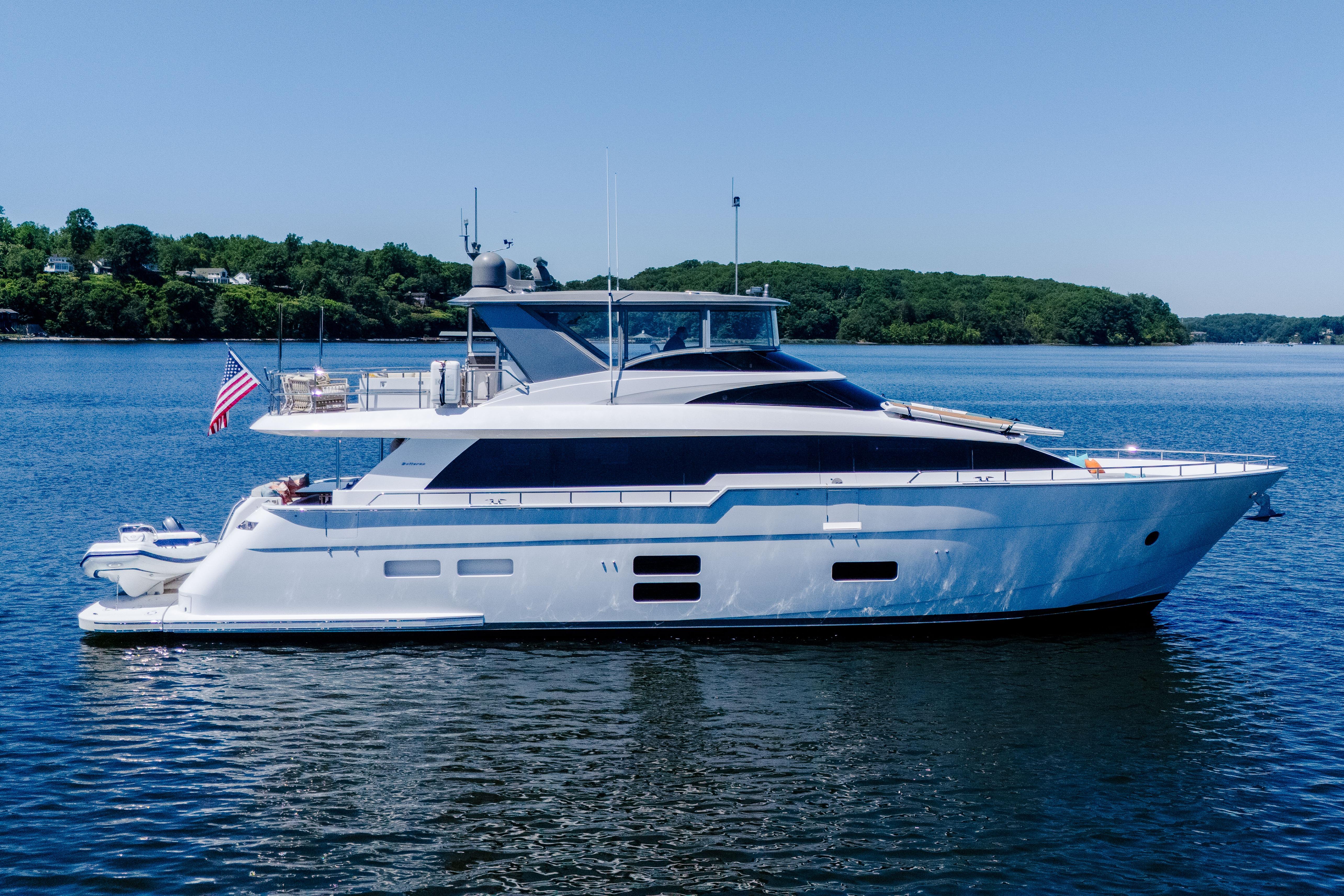 2021 Hatteras M75 Panacera yacht on serene water with lush green shoreline.