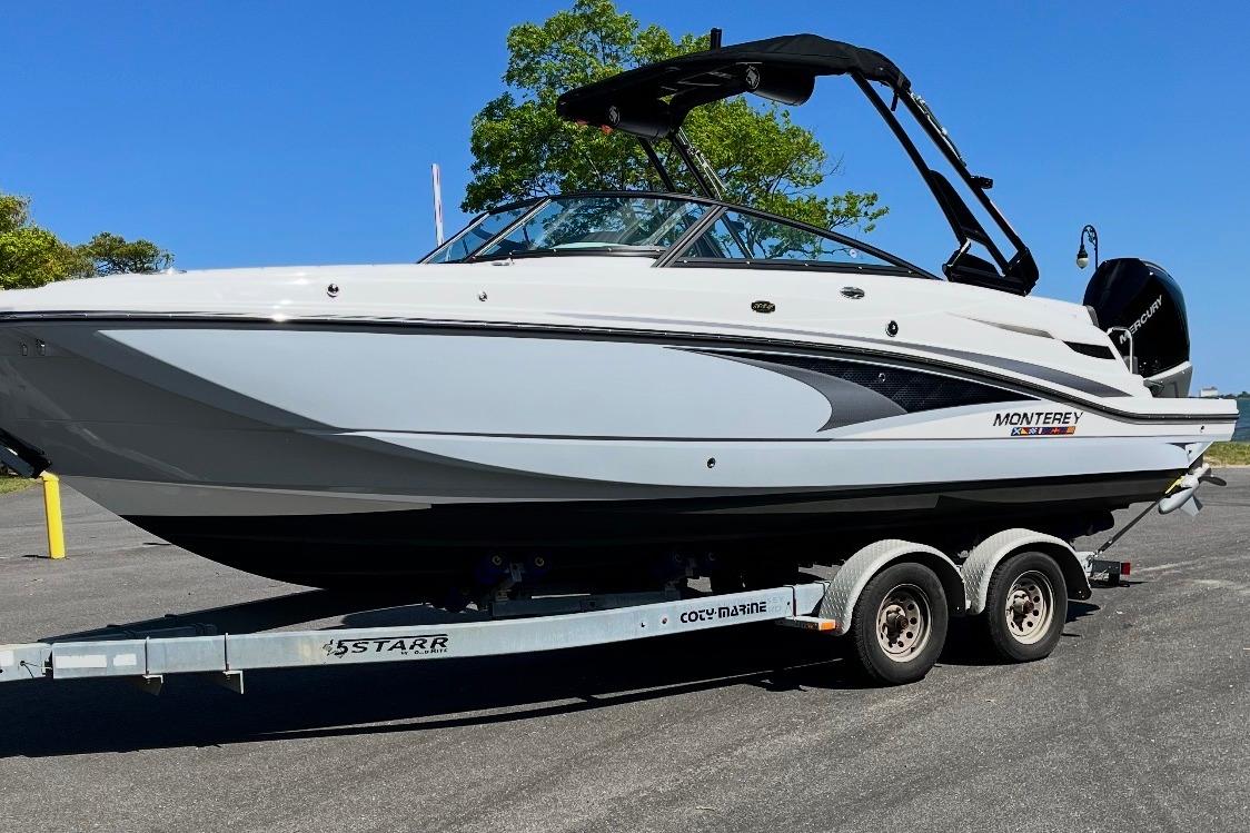 2024 Monterey M-65 boat on trailer, sleek design, parked outdoors under clear blue sky.