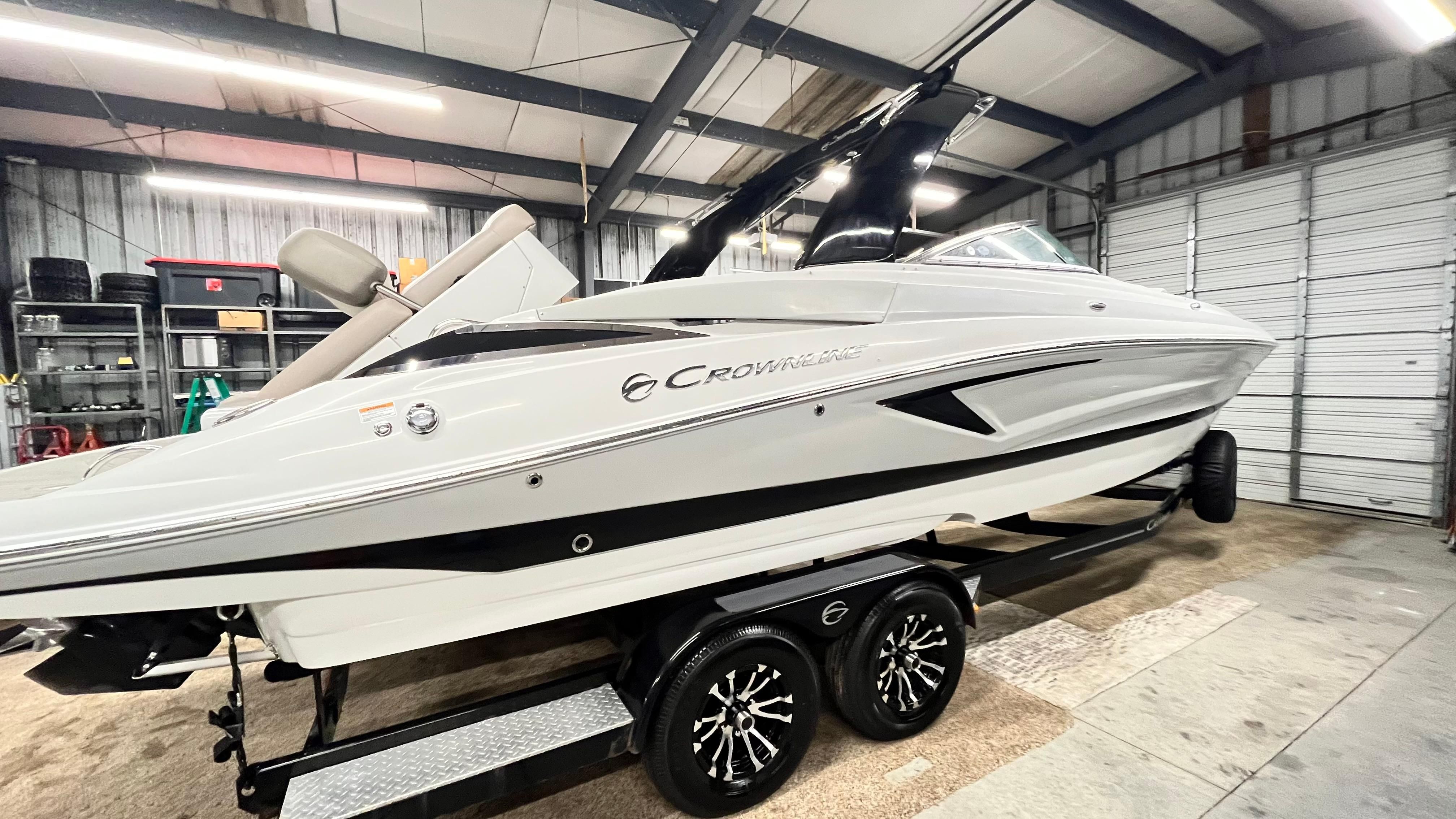 A white 2019 Crownline E 285 boat is on a trailer inside a warehouse.