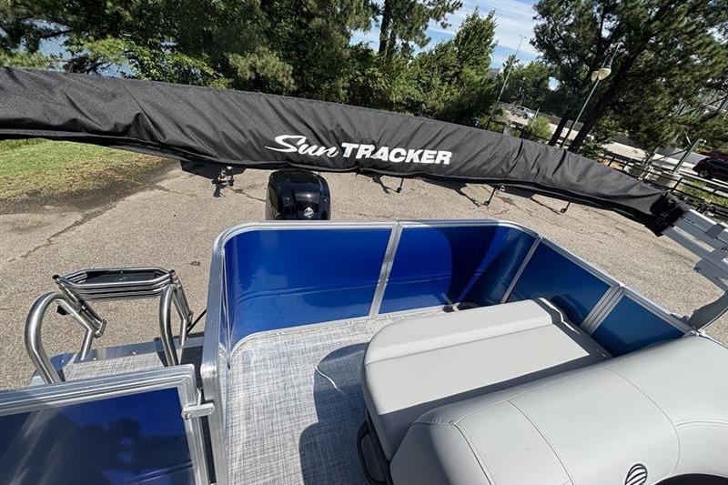 2026 Sun Tracker Party Barge 18 DLX pontoon boat with seating, docked near trees.
