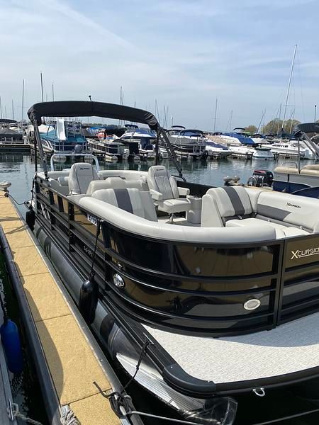 A 2020 Xcursion 243 RFX pontoon boat docked. It features black railings and gray seating.
