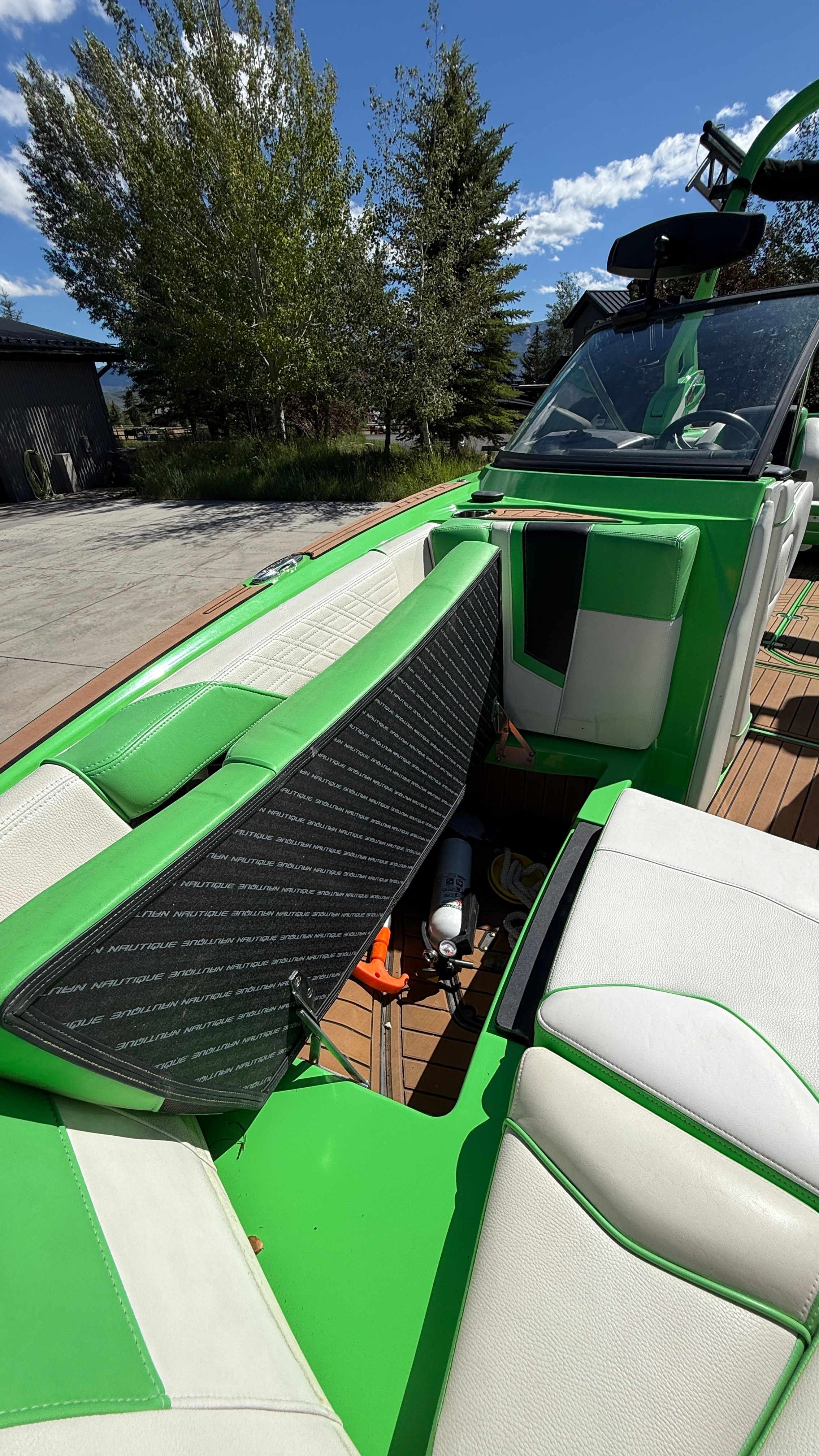 Green and white boat with seating area and storage, surrounded by trees.