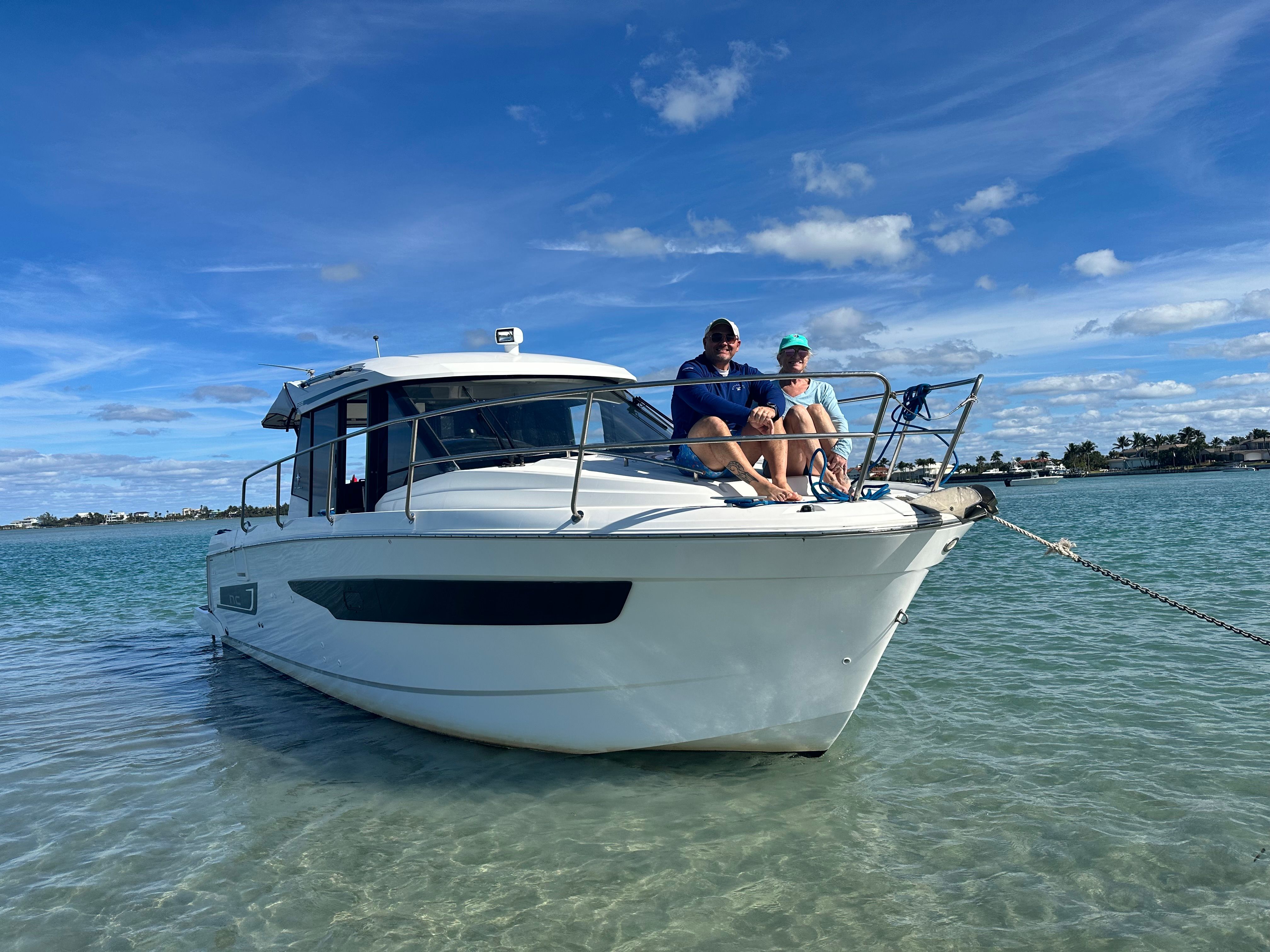 Two people sit on a white Jeanneau NC 895 boat in clear water.