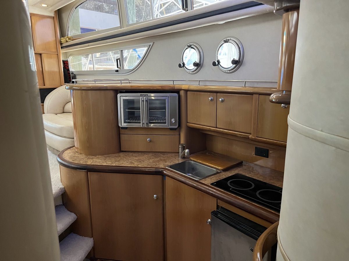 The galley of a 1999 Sealine F44 with wooden cabinets, sink, stove, and microwave.