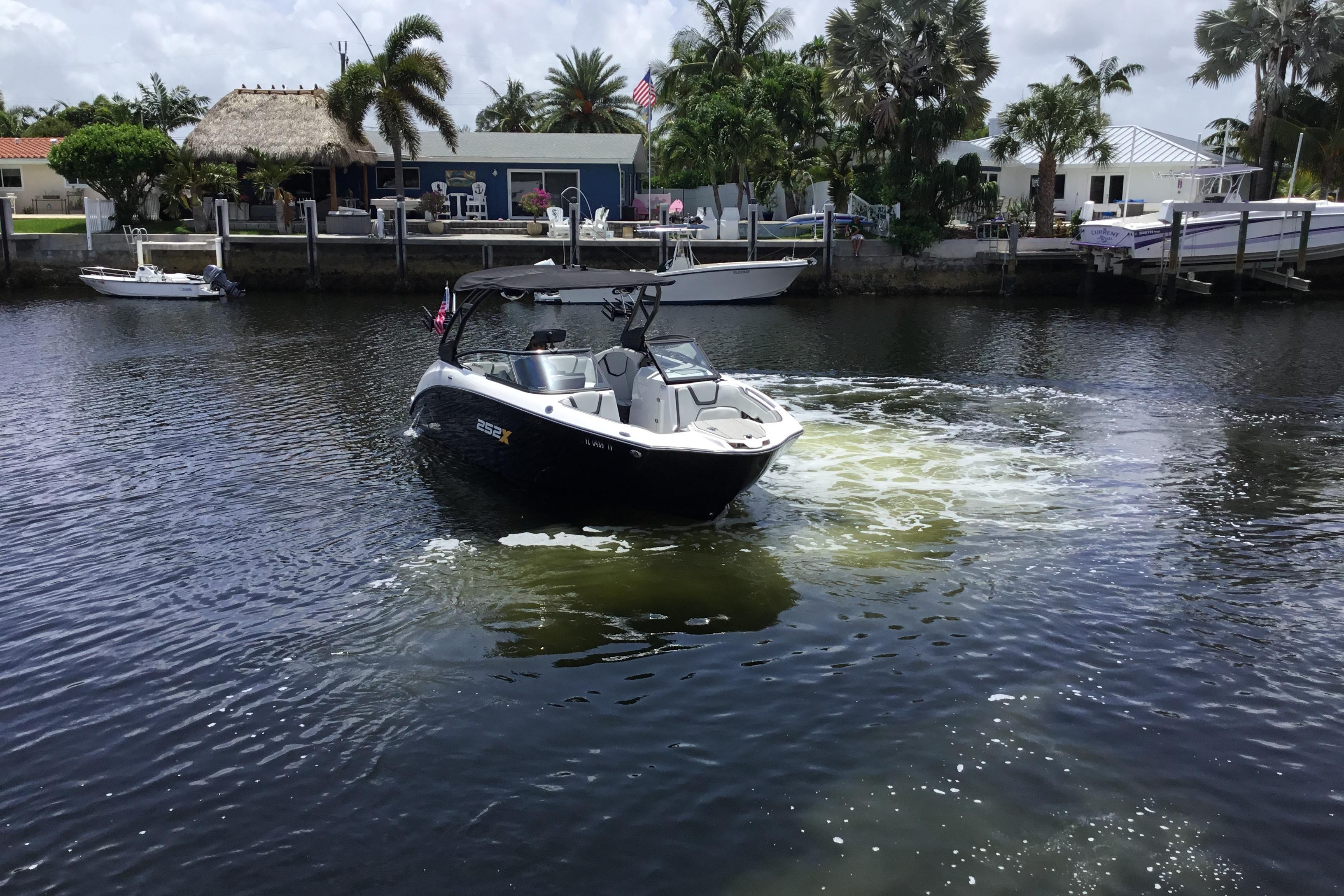 2023 Yamaha Boats 252XE navigating a scenic canal with waterfront homes and palm trees.