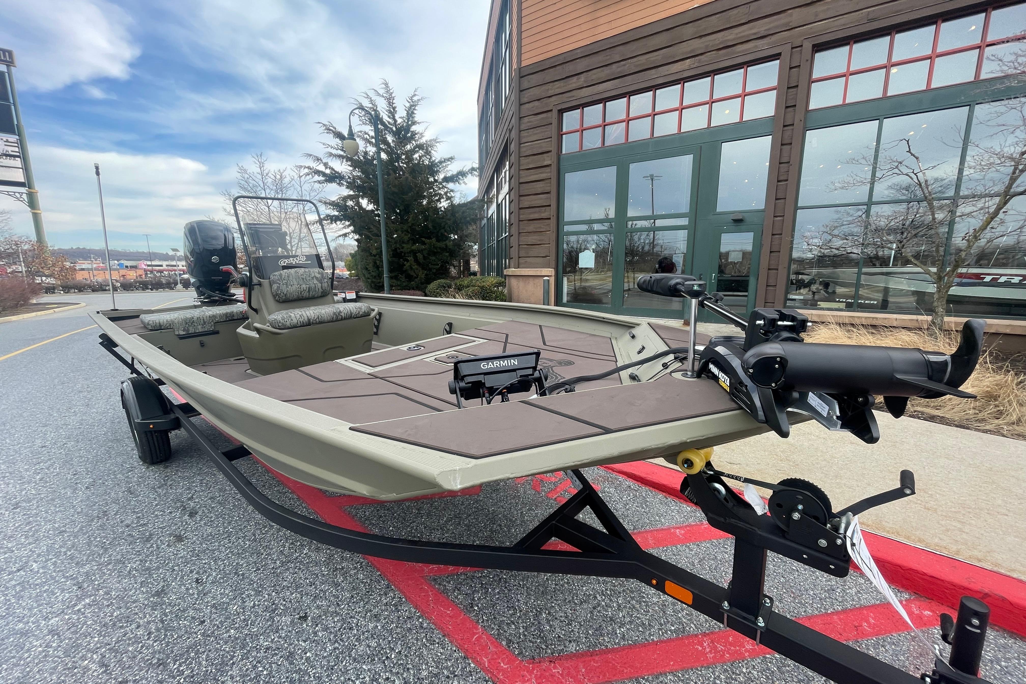 2026 Tracker Grizzly 1860 CC boat on trailer, parked outside a building.