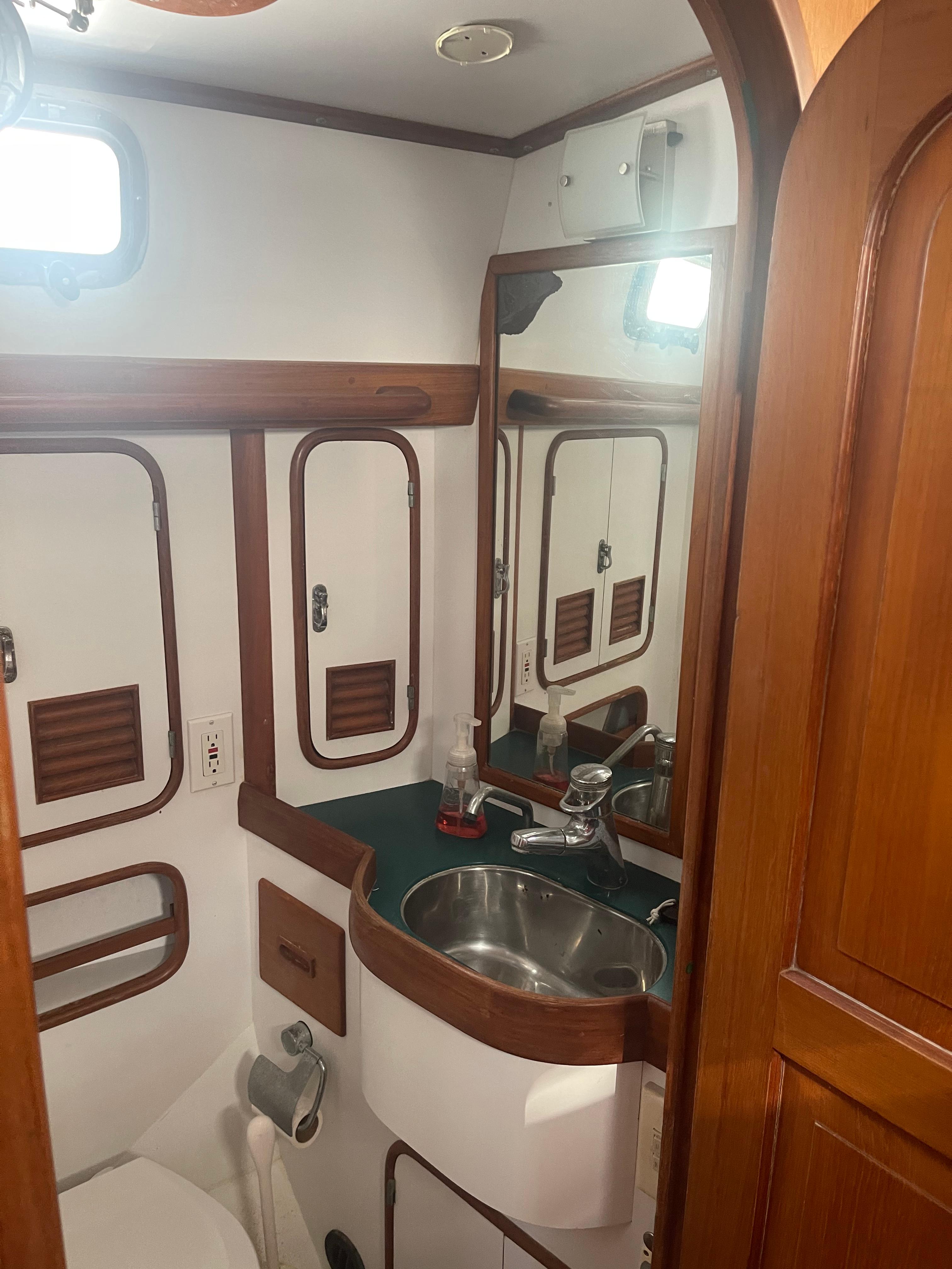 1995 Passport 47 AC Plan B yacht bathroom with sink, mirror, and wooden cabinetry.