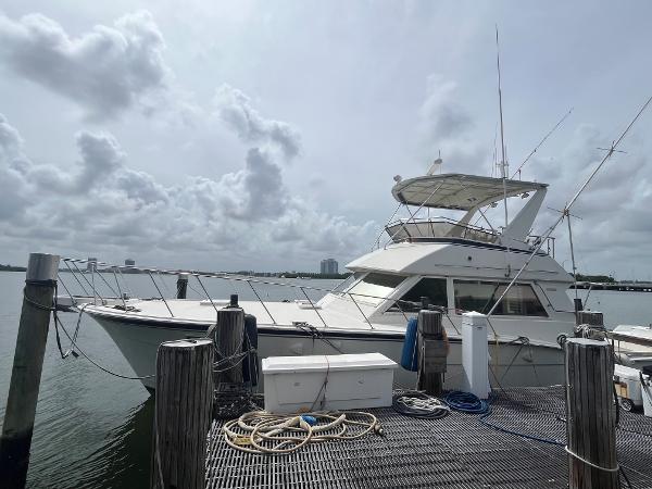 1985 Hatteras 45 Convertible yacht docked at marina under cloudy sky.
