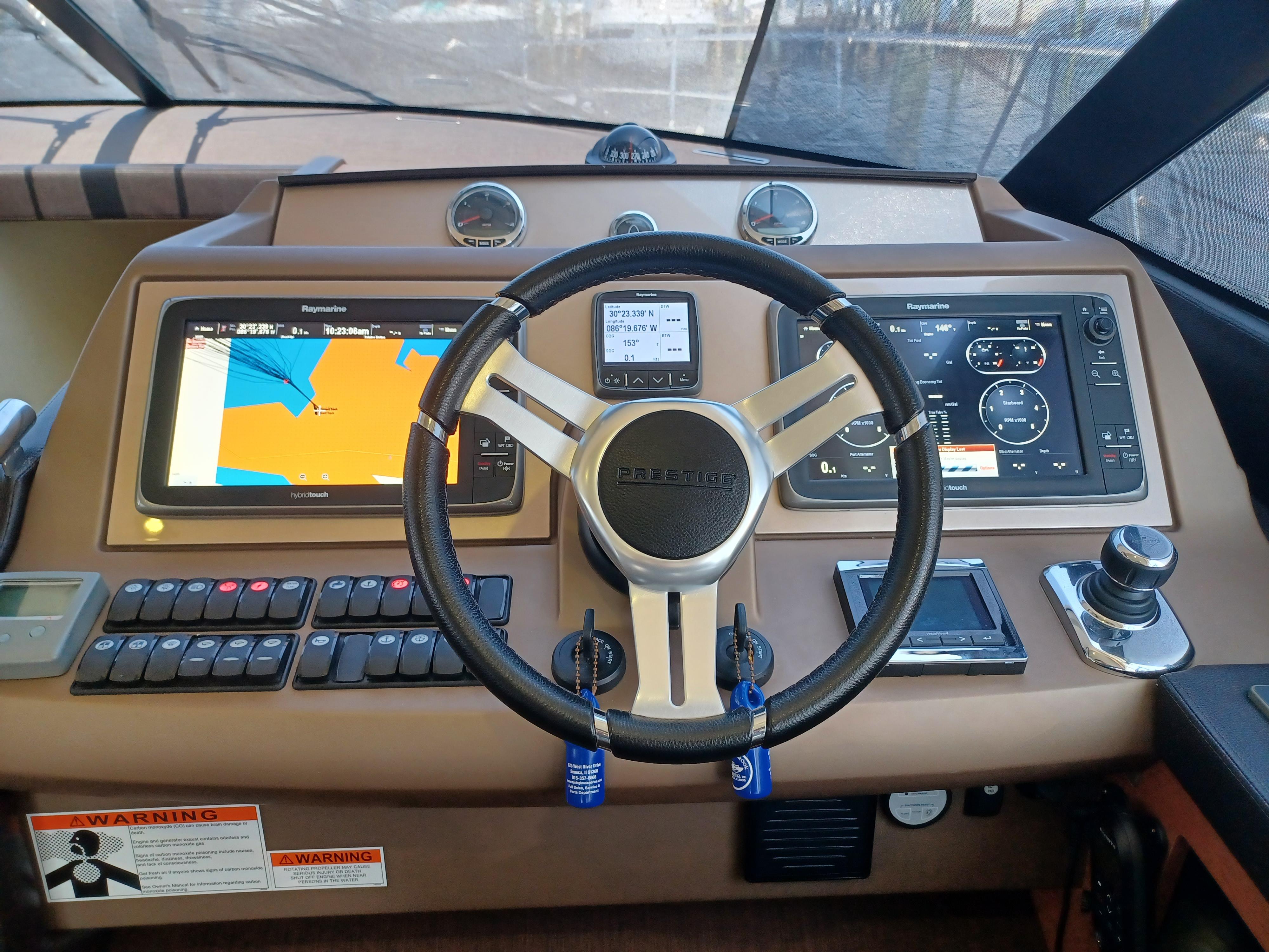 Control panel of a 2015 Prestige 550 Flybridge yacht with navigation screens and steering wheel.