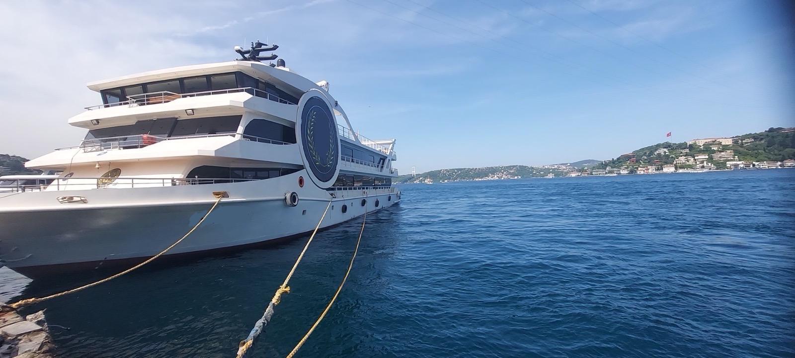 Luxury Custom-Craft restaurant vessel docked by the sea, 2025 model, with scenic coastal backdrop.