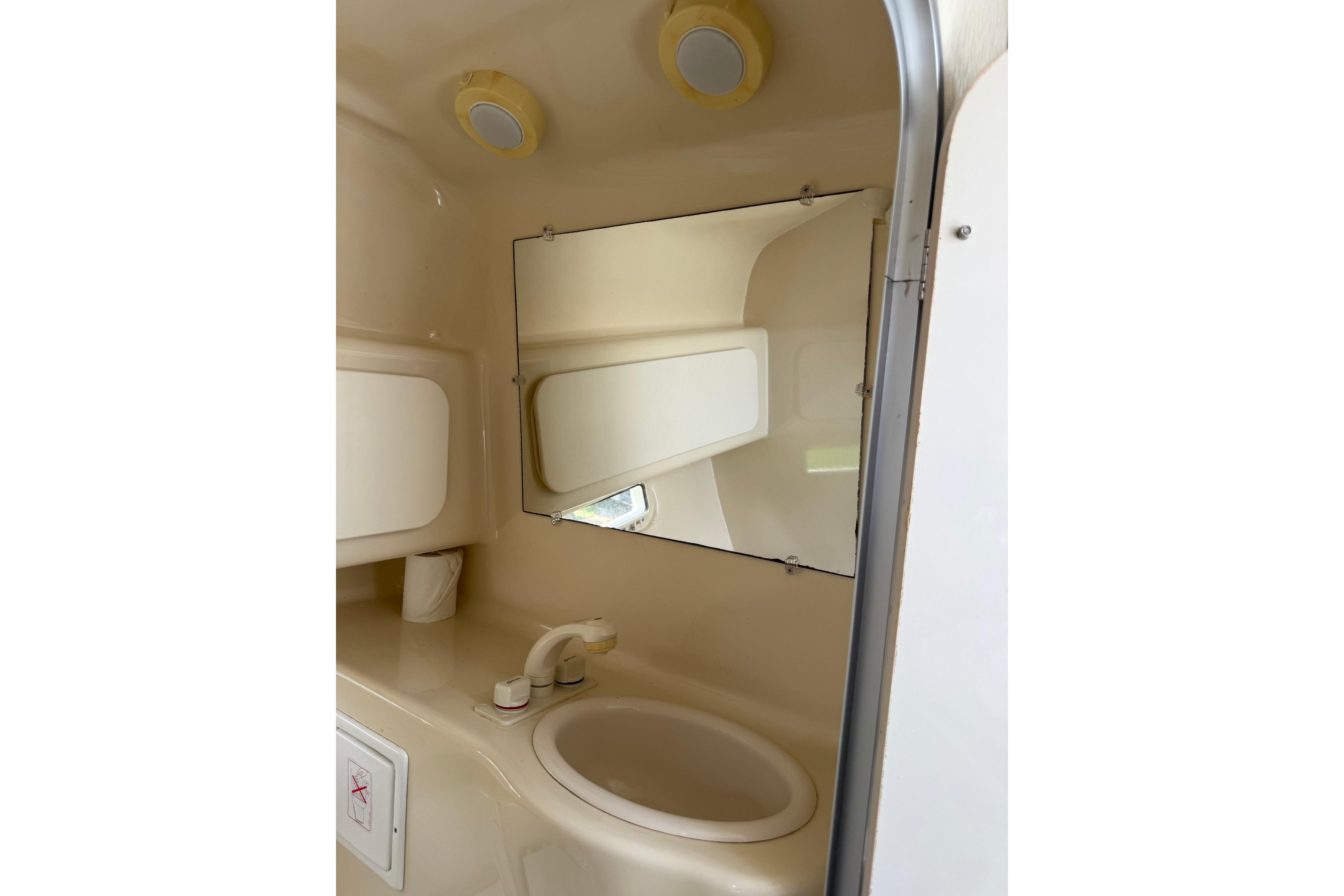 Compact bathroom in 2000 Maxum 2400 SCR boat with sink, mirror, and storage.