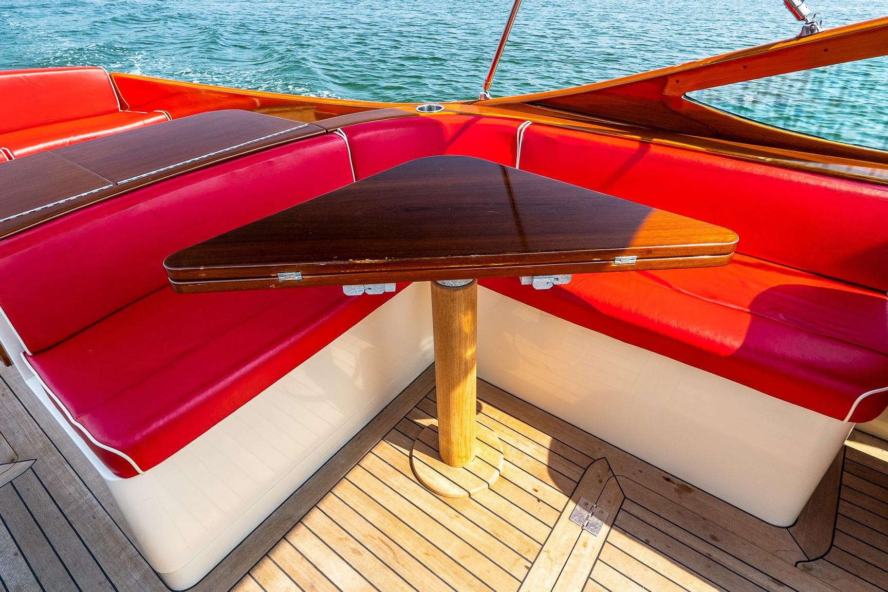 Luxury seating area on 2005 Hinckley Talaria 29R boat with red cushions and wooden table.