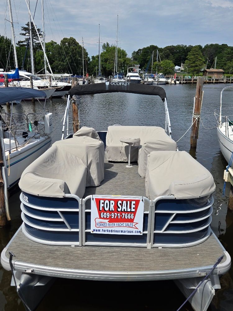 A 2022 Godfrey Sweetwater 2186C pontoon boat is docked, featuring a 'For Sale' sign.