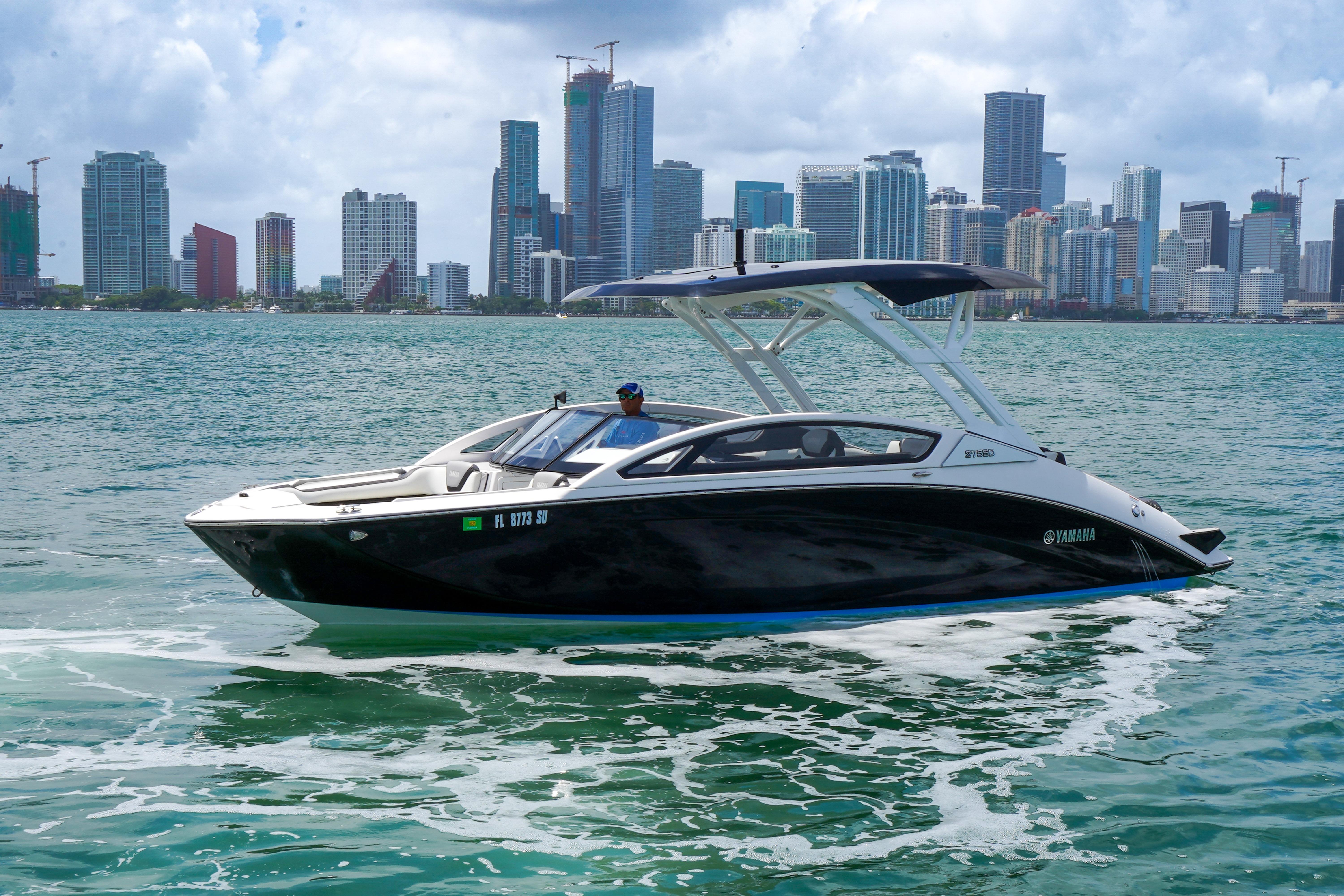 2021 Yamaha Boats 275SD cruising on water with city skyline backdrop.