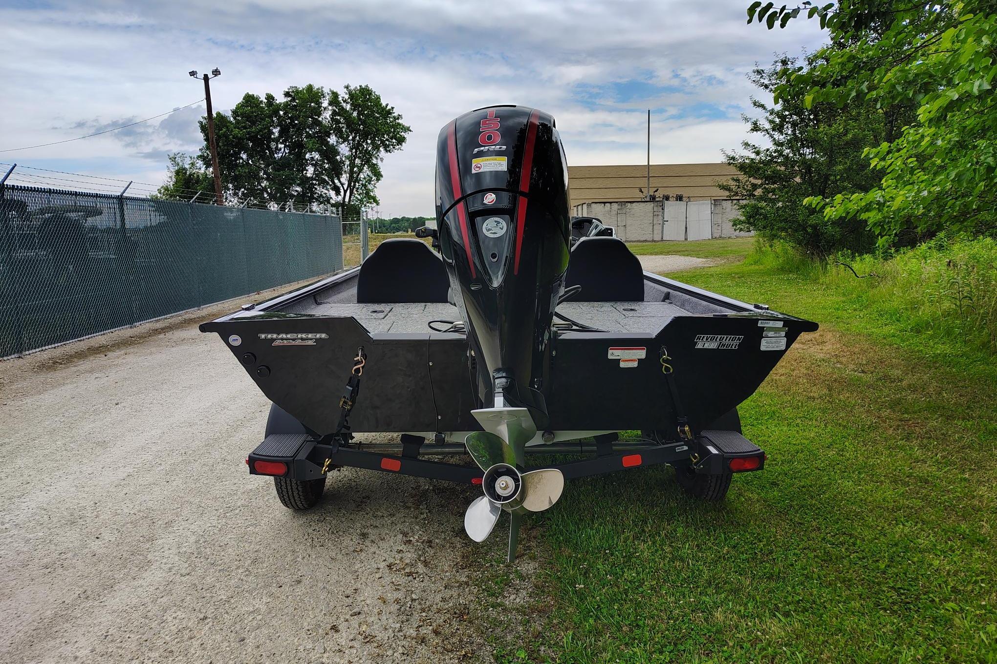 2026 Tracker Pro Team 195 boat on trailer, parked on gravel path near greenery.