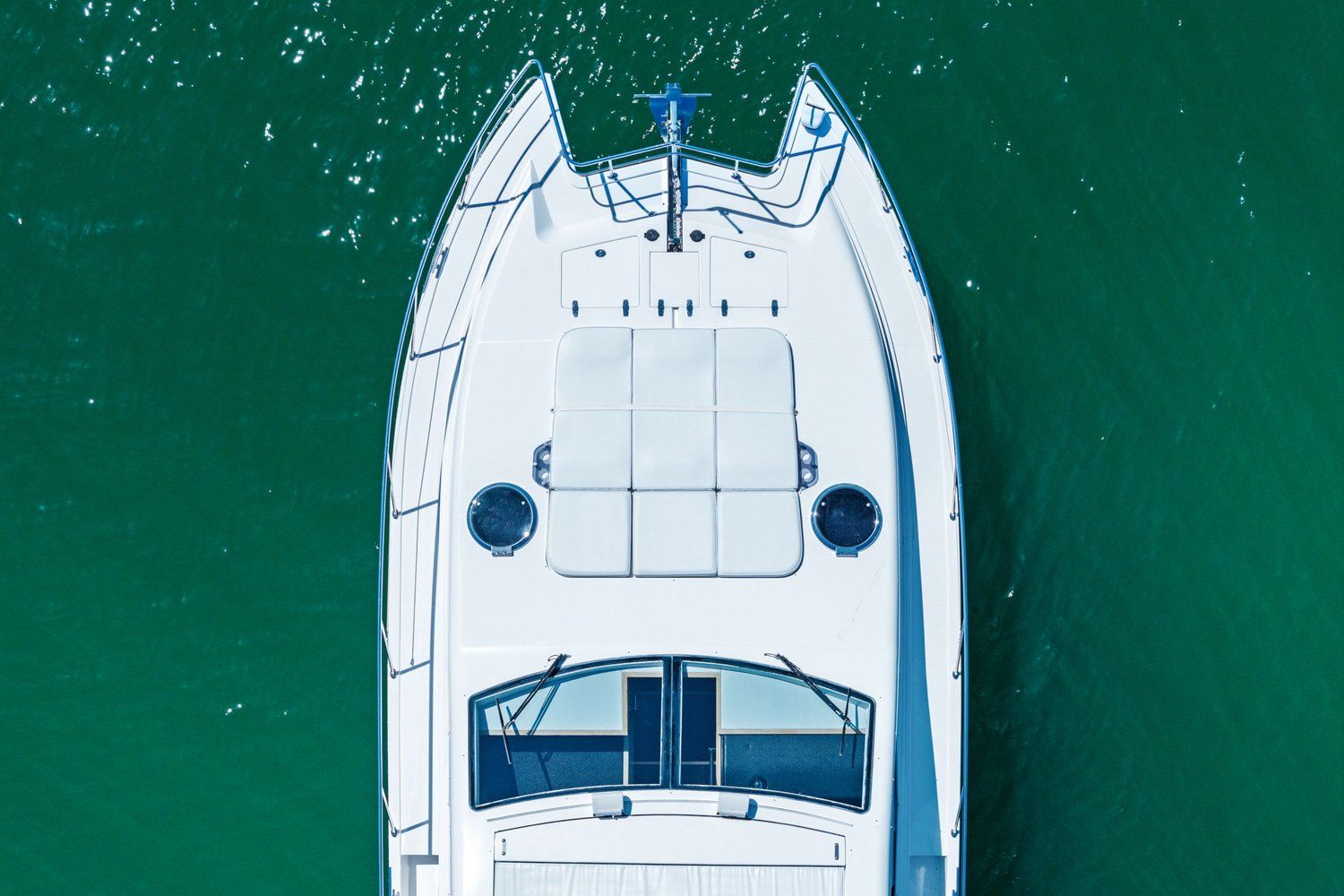 Aerial view of a white catamaran on green water with spacious deck and windows.