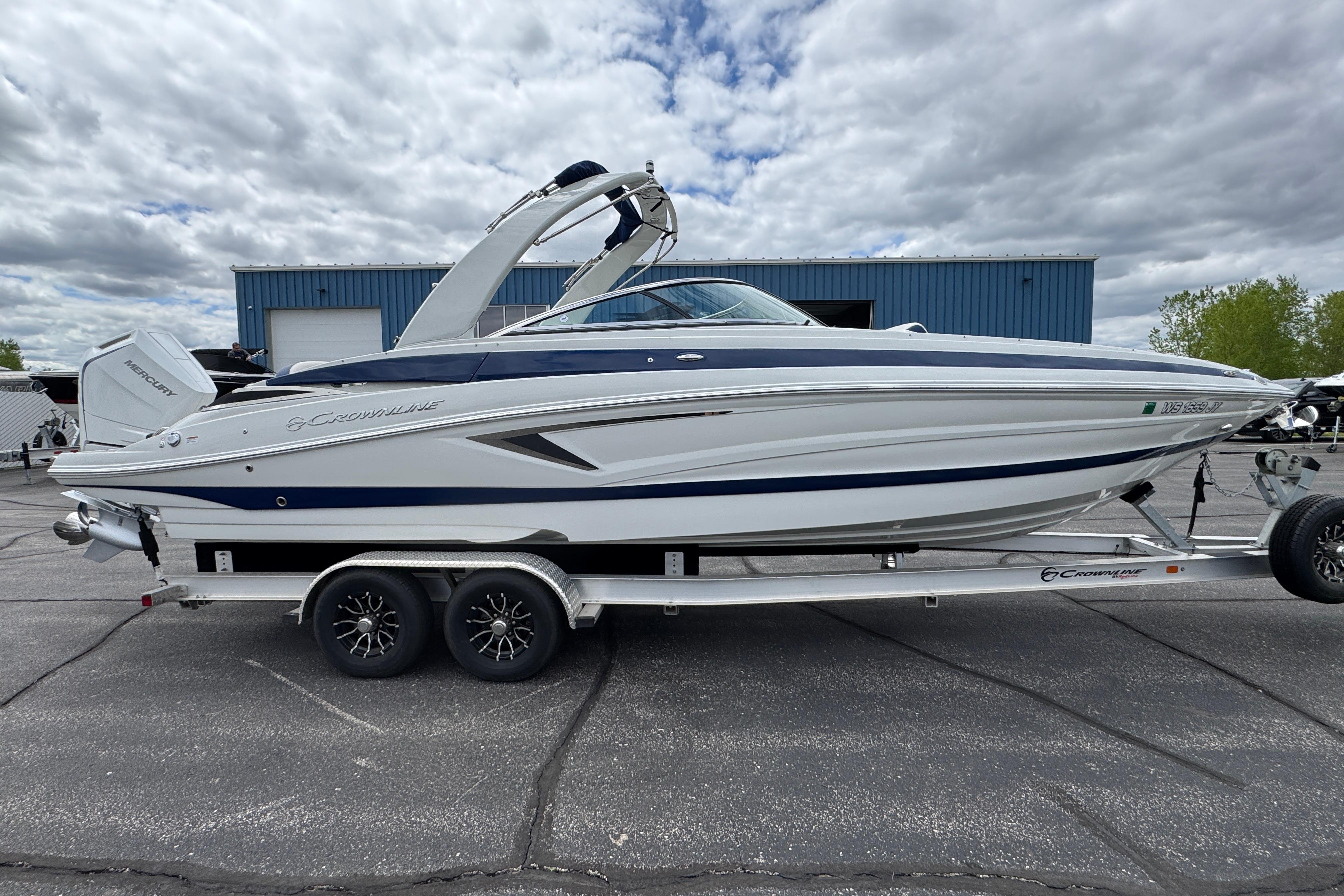 2025 Crownline 290 XSS boat on trailer, parked outdoors under cloudy sky.