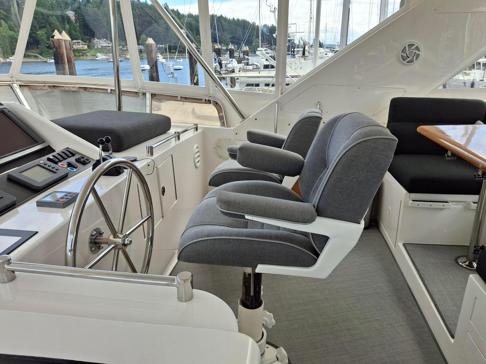 Pilothouse interior of 2004 Ocean Alexander 64, featuring helm, seating, and scenic marina view.