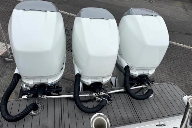 Triple outboard motors on a 2016 Mystic M4200 boat, docked on a wooden platform.