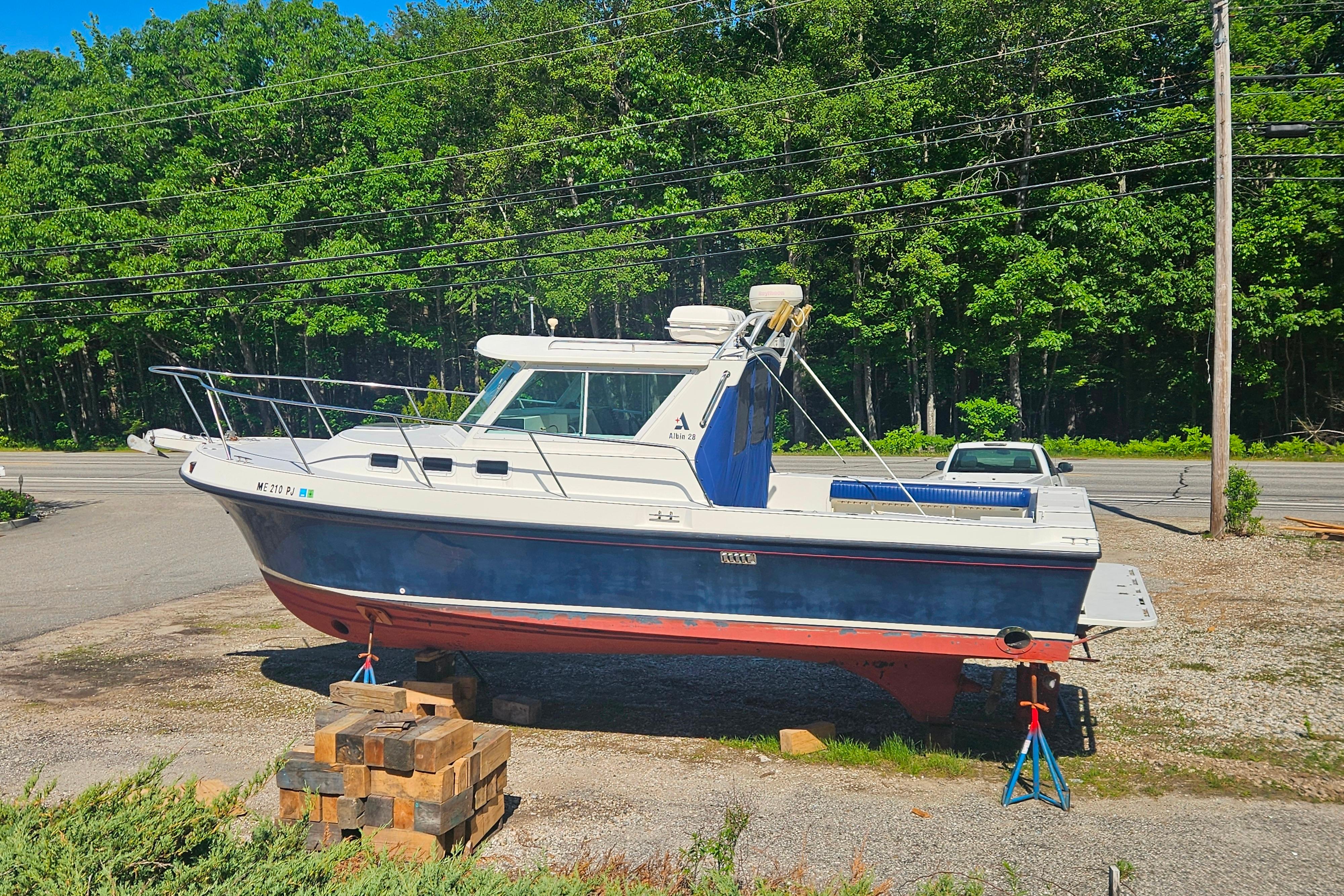 1999 Albin 28 Tournament Express boat on land, surrounded by trees and parked cars.