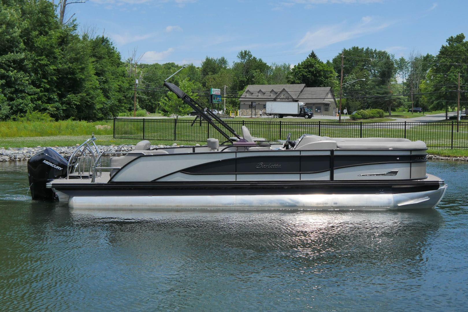 2023 Barletta CORSA 25UE pontoon boat on a calm lake, surrounded by greenery.