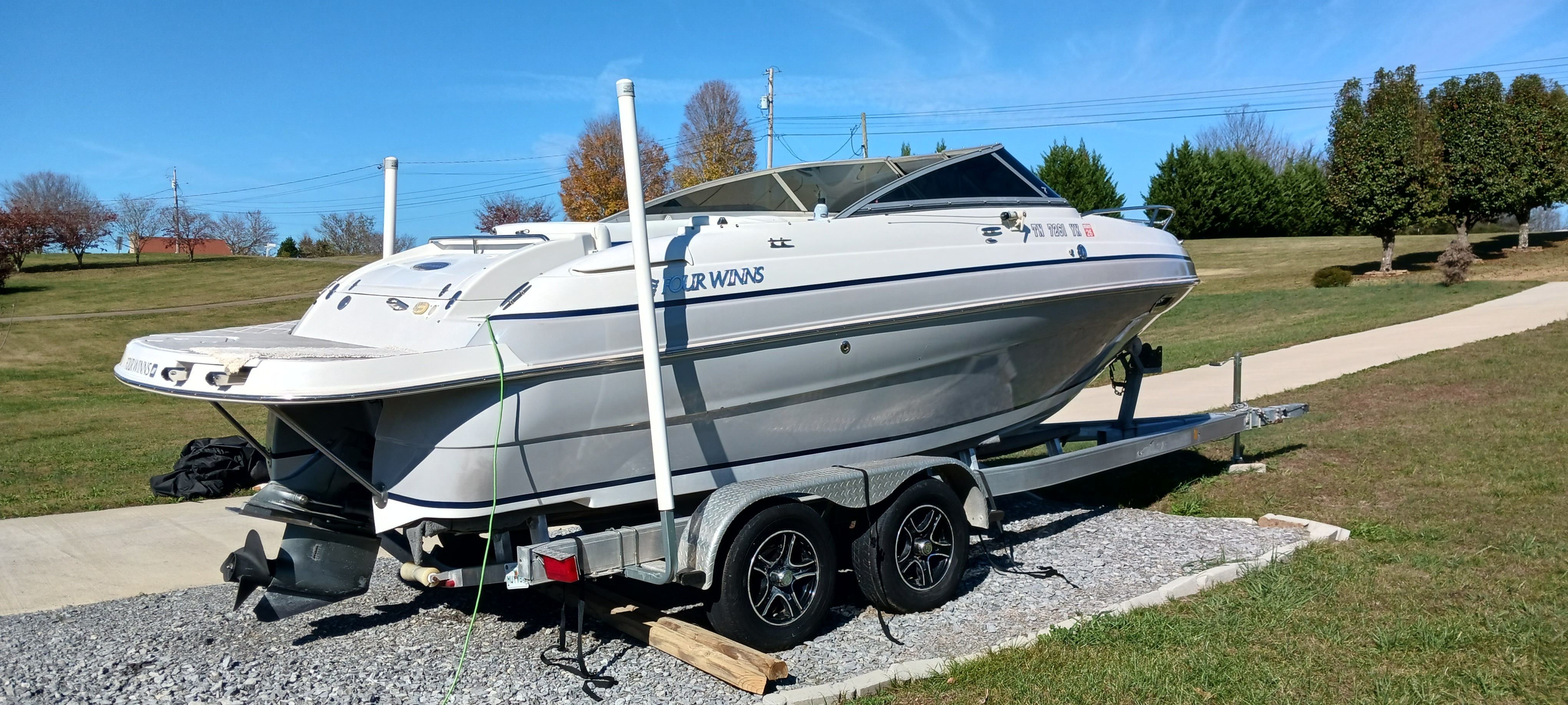 2003 Four Winns 205 Sundowner boat on trailer, parked on gravel driveway, under clear blue sky.