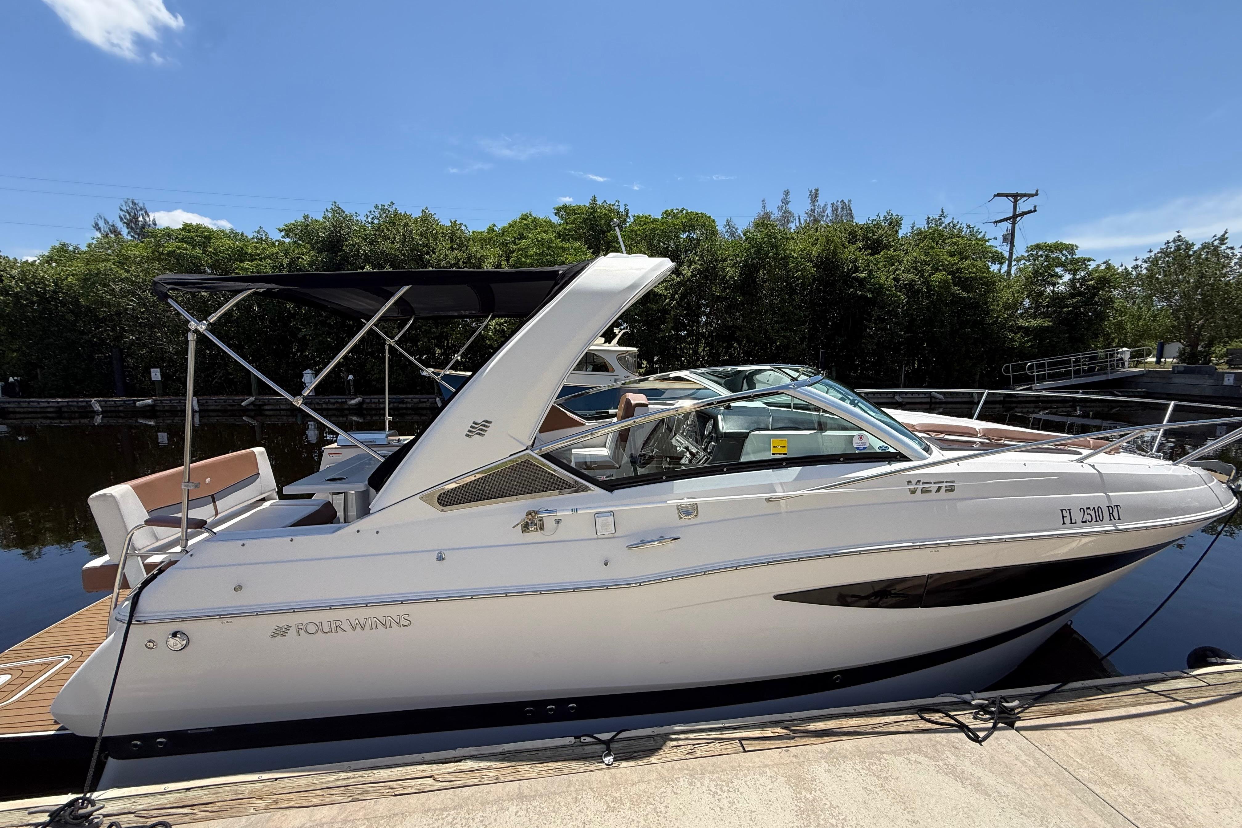 2017 Four Winns V275 boat docked, featuring sleek design and canopy, under clear blue sky.