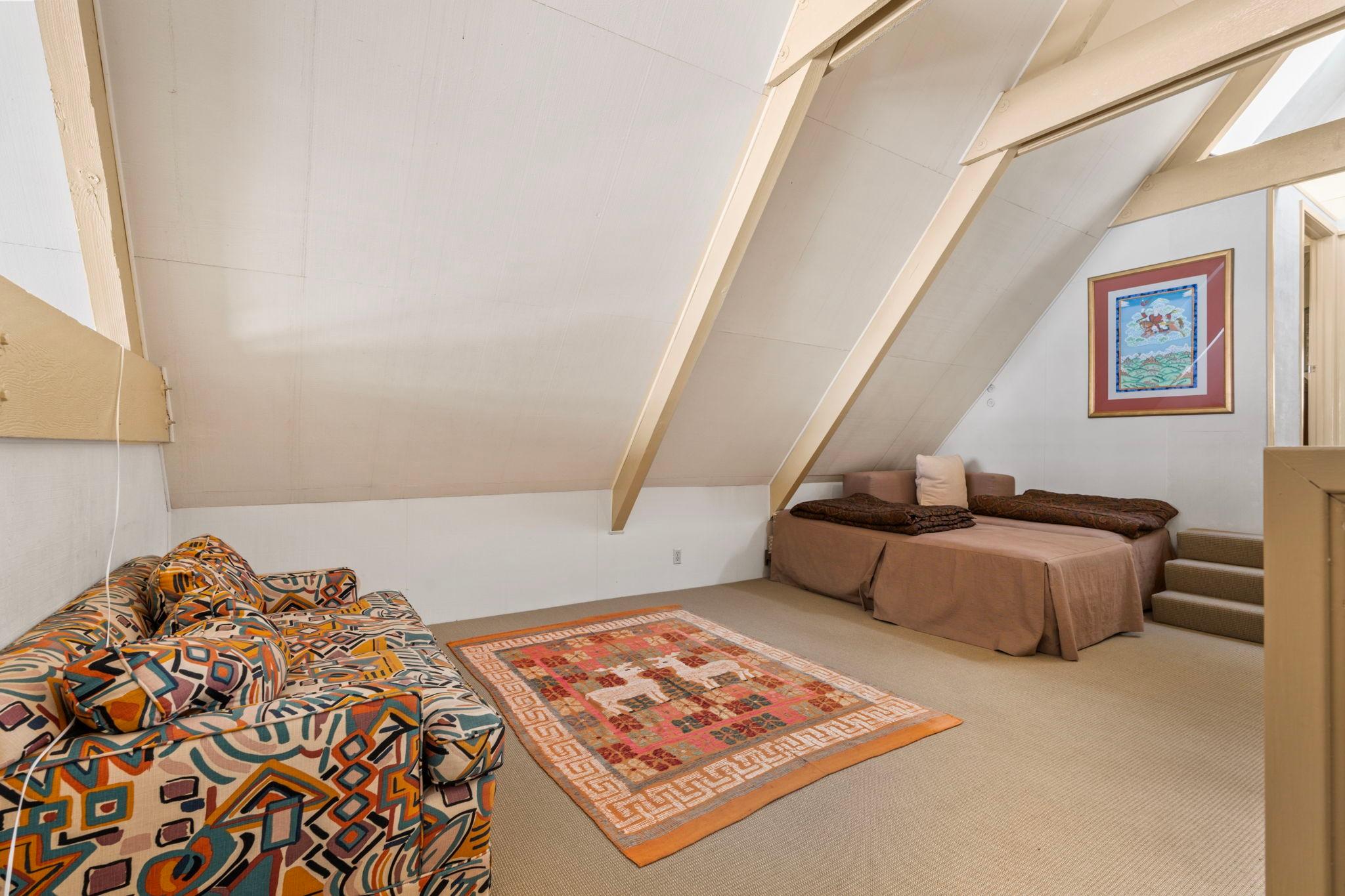 A-frame attic room with patterned sofa, colorful rug, and bed, in a 1976 custom boathouse.
