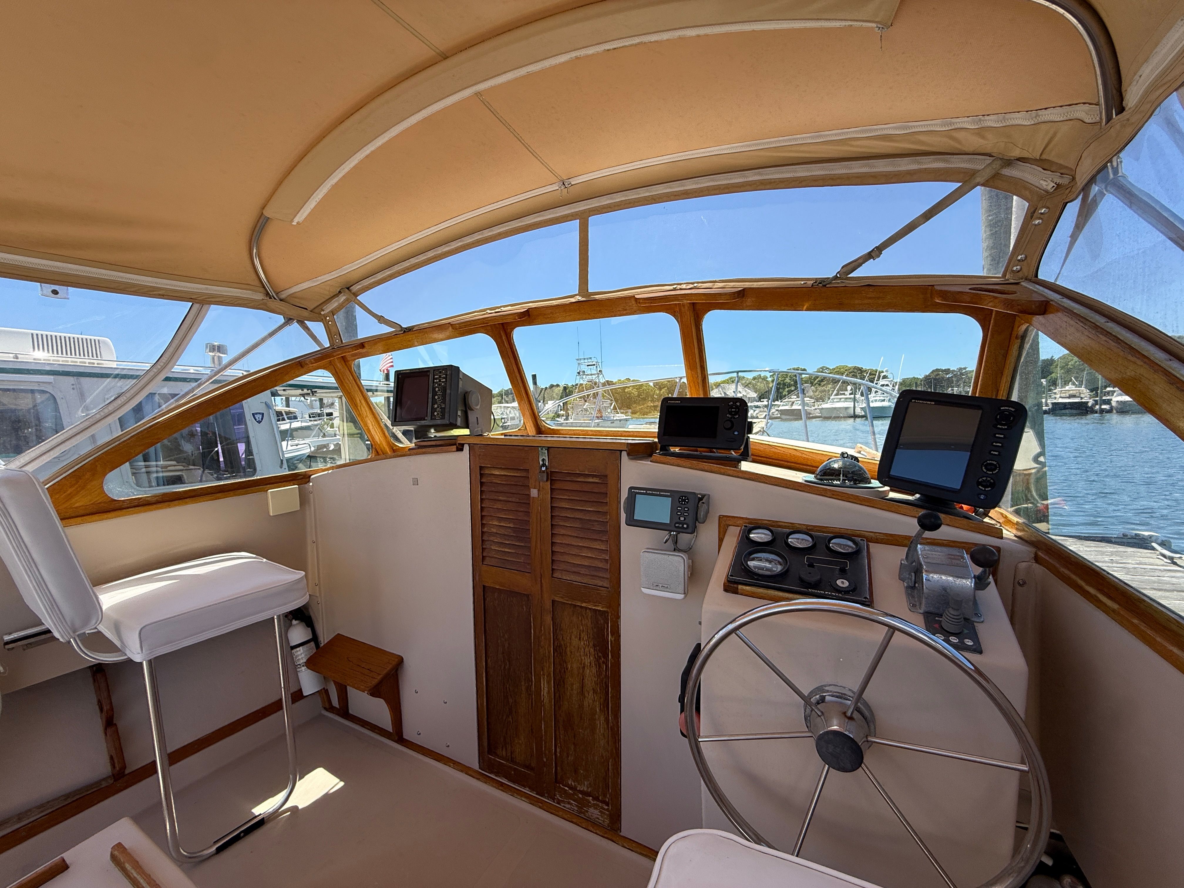 Interior view of a boat with steering wheel and navigation equipment, docked at a harbor.