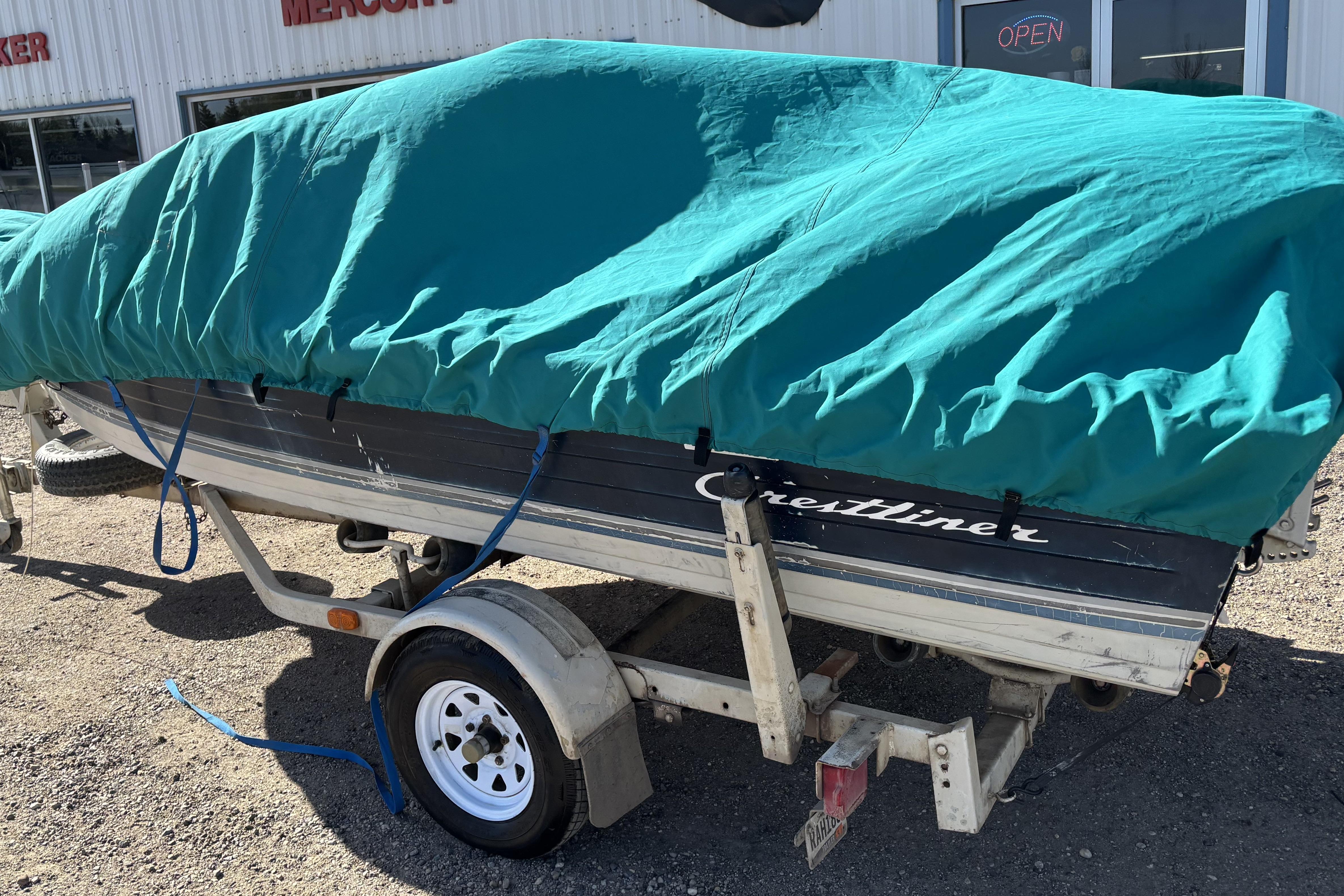 1983 Crestliner 16 boat covered with a teal tarp on a trailer.