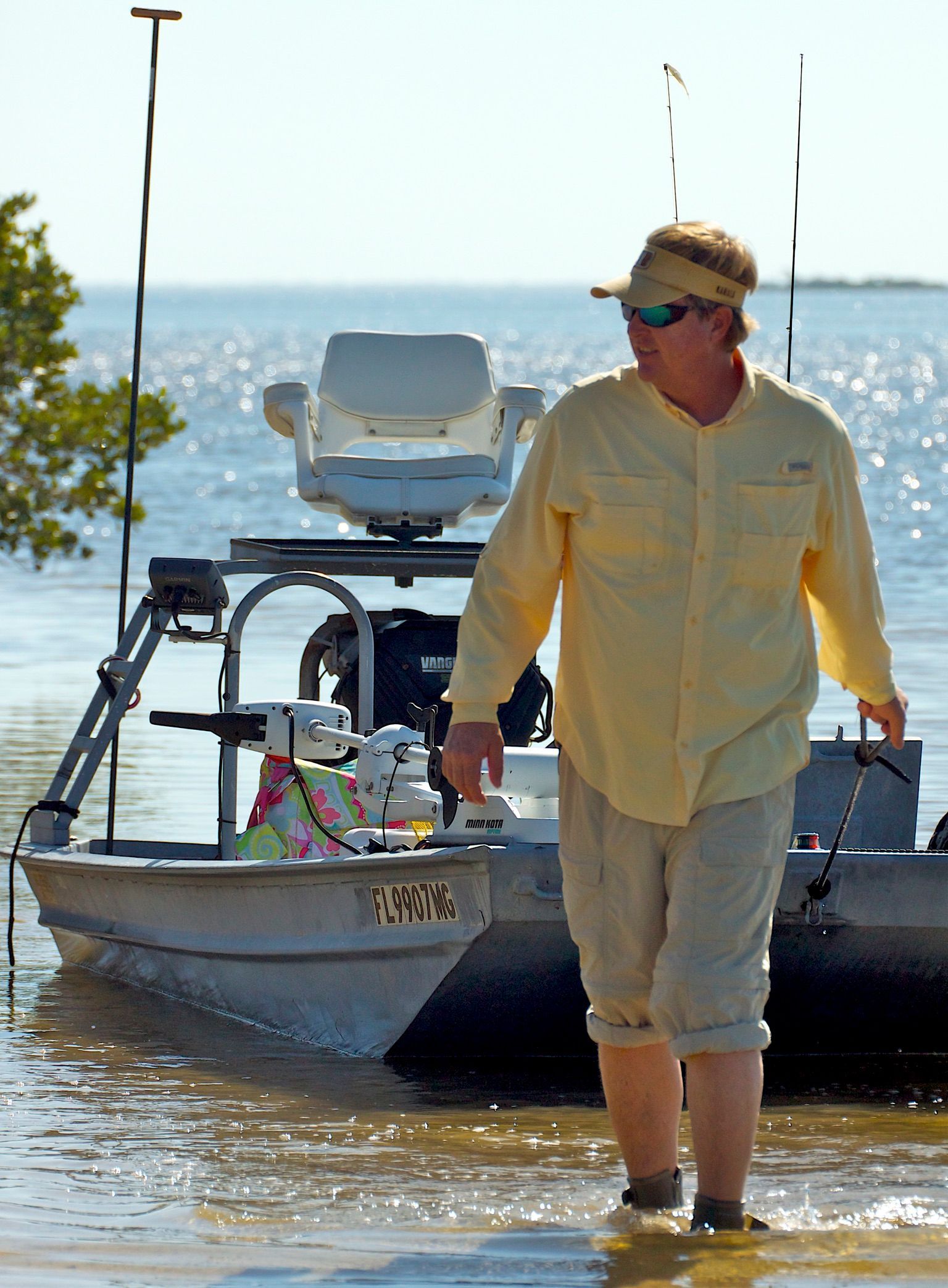 A man stands beside a 2003 Go-Devil 16x56 fishing boat in shallow water.