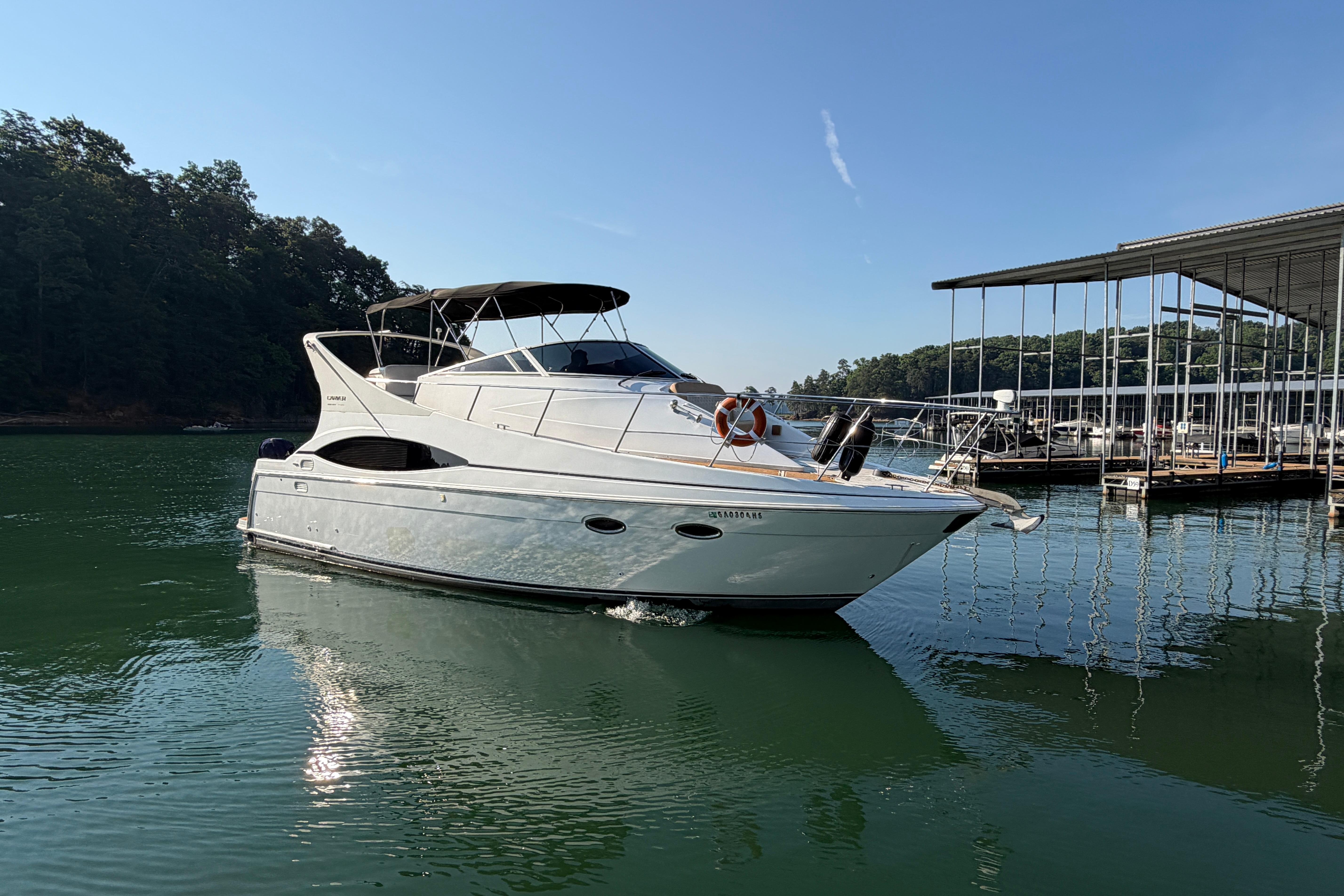2003 Carver 350 Mariner yacht on calm water near a marina, under clear blue sky.