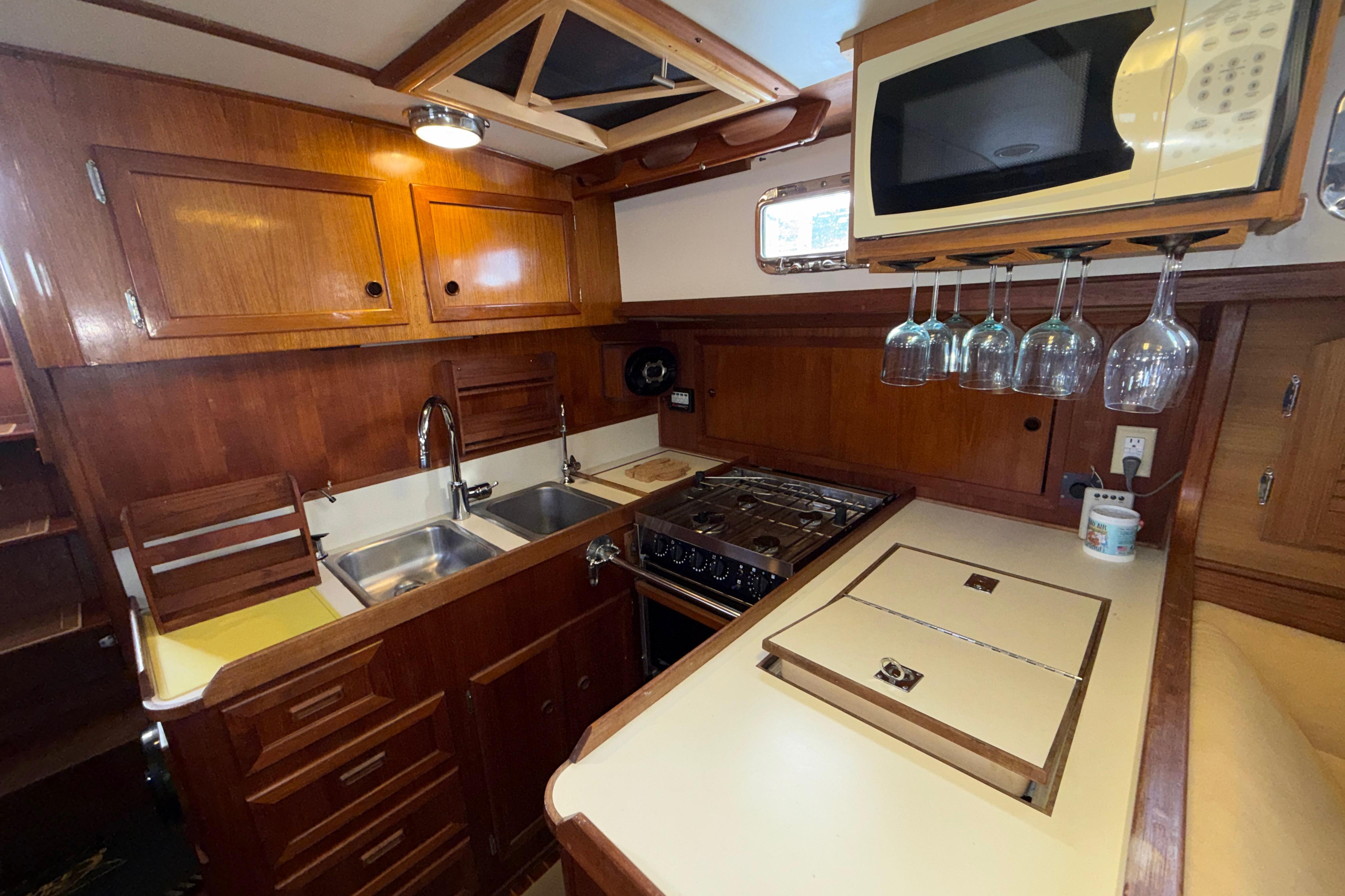 1983 Valiant Cutter yacht kitchen with wooden cabinets, stove, and hanging wine glasses.