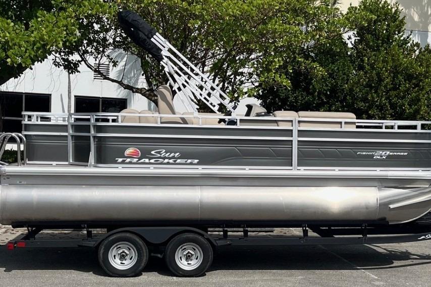 2025 Sun Tracker Fishin' Barge 20 DLX pontoon boat on trailer, parked outdoors.