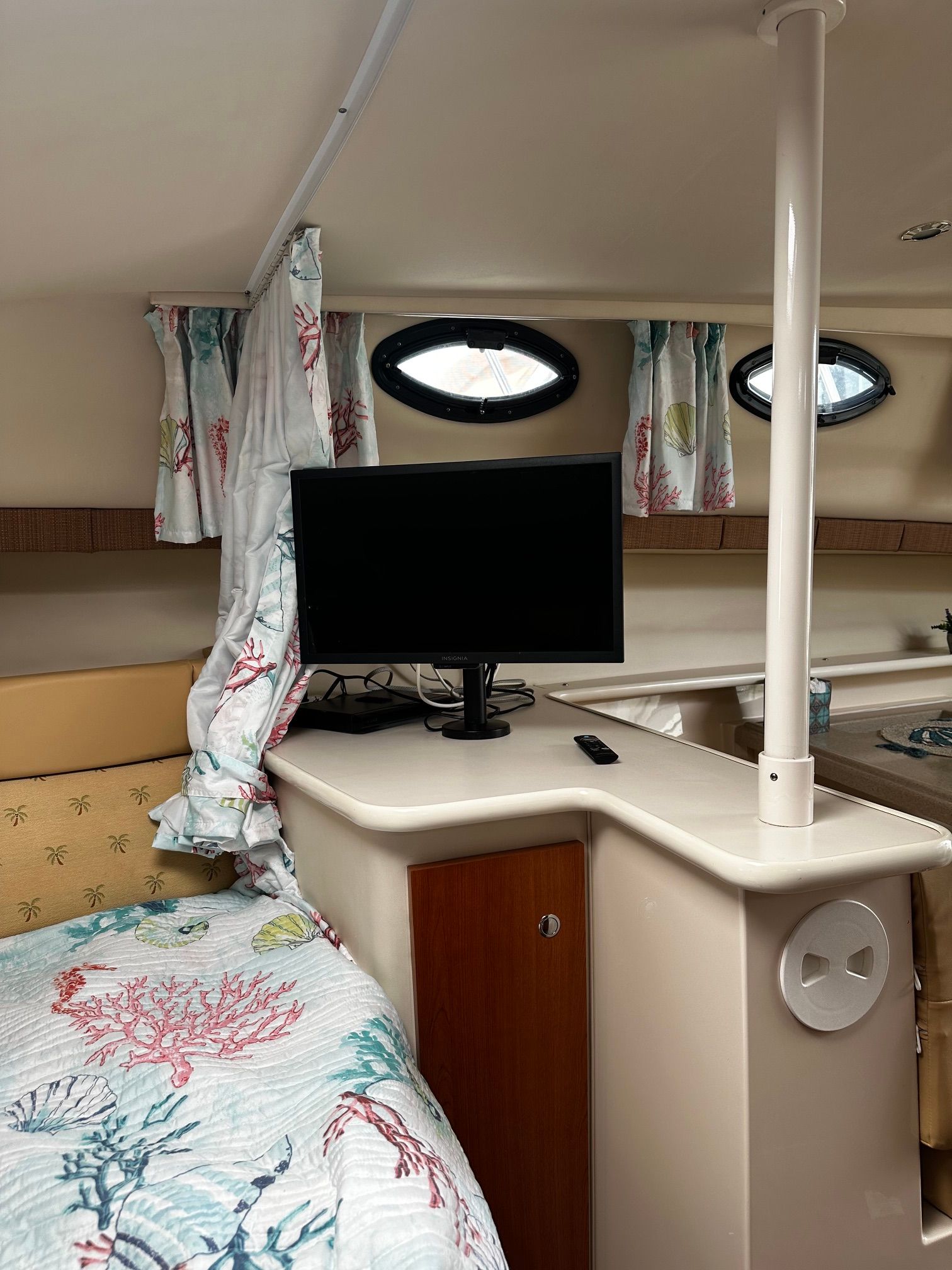 Interior of a Wellcraft 330 Coastal with bed, TV, and nautical-themed curtains.