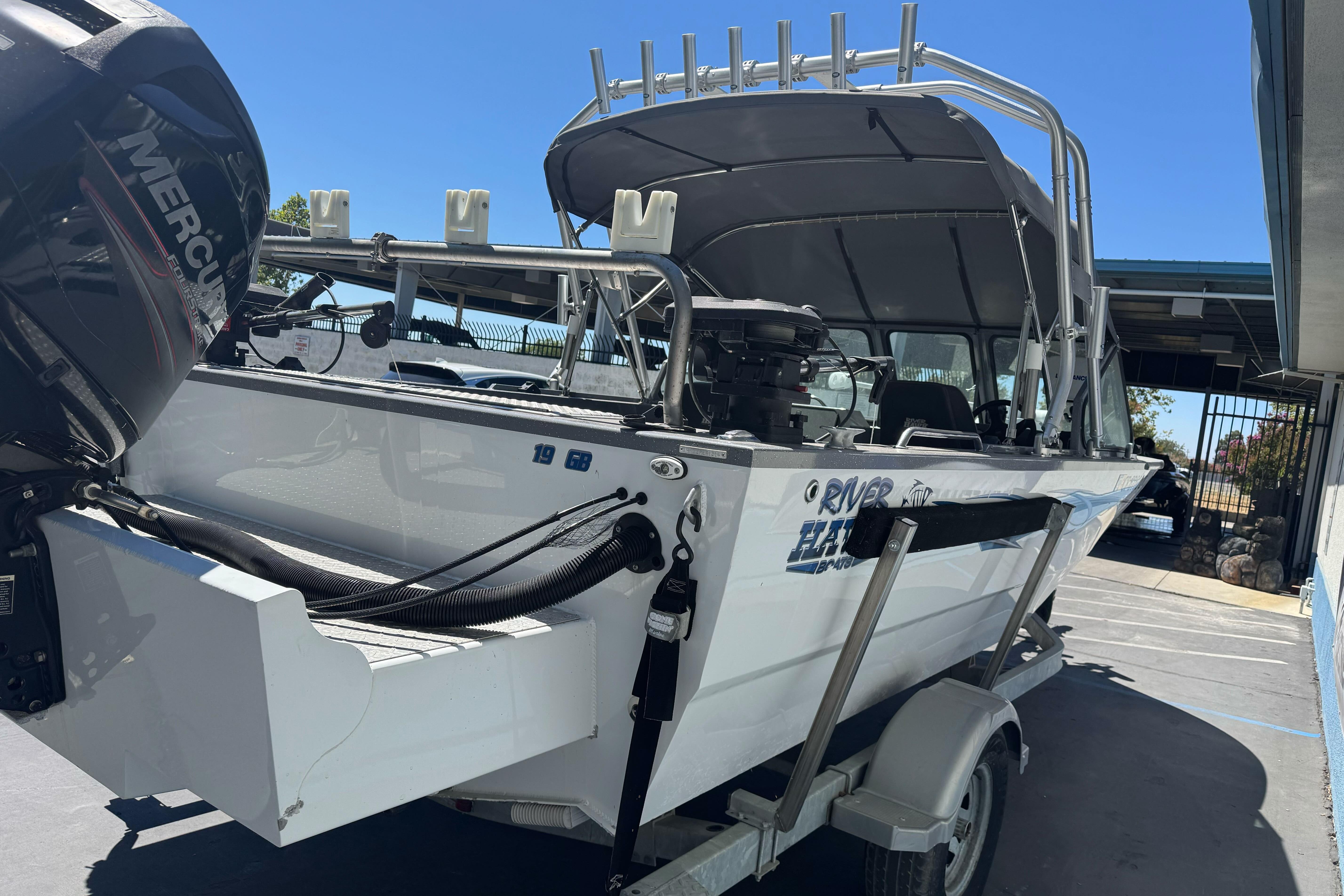 2014 River Hawk 19 GB boat with Mercury engine on trailer, parked outdoors.