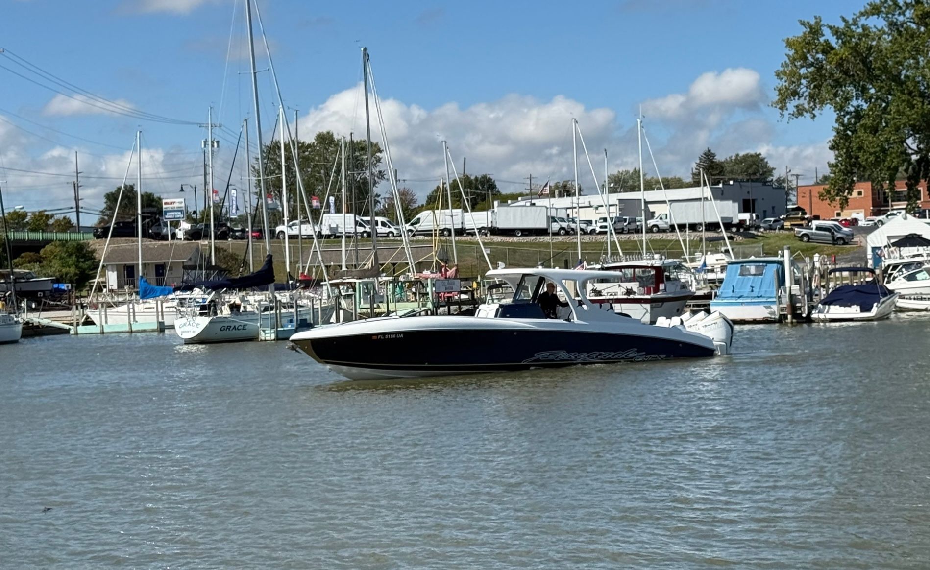 A black motorboat cruises in a busy harbor with numerous sailboats in the background.